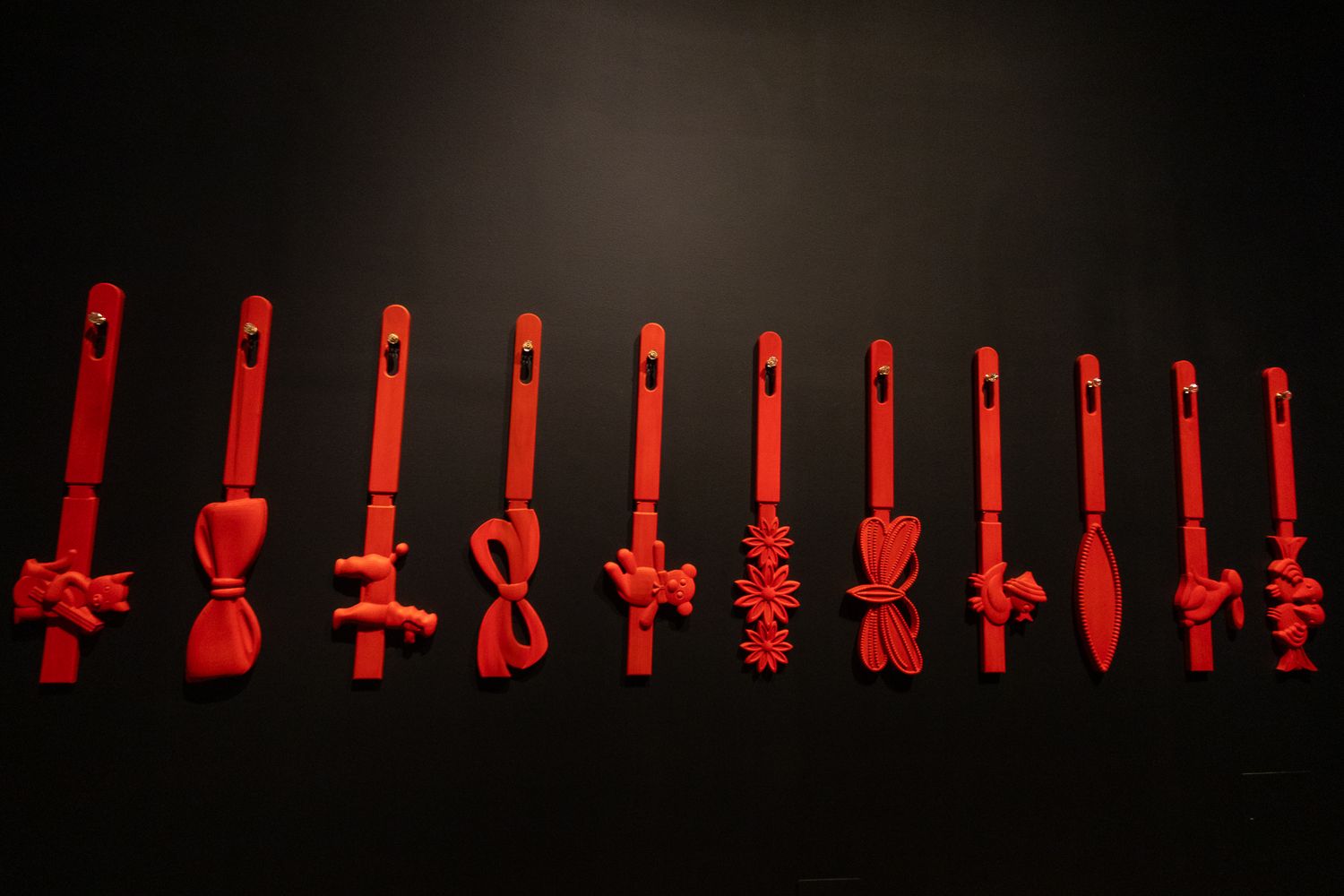 Red plastic utensils with decorative knots arranged in a row against a dark background.