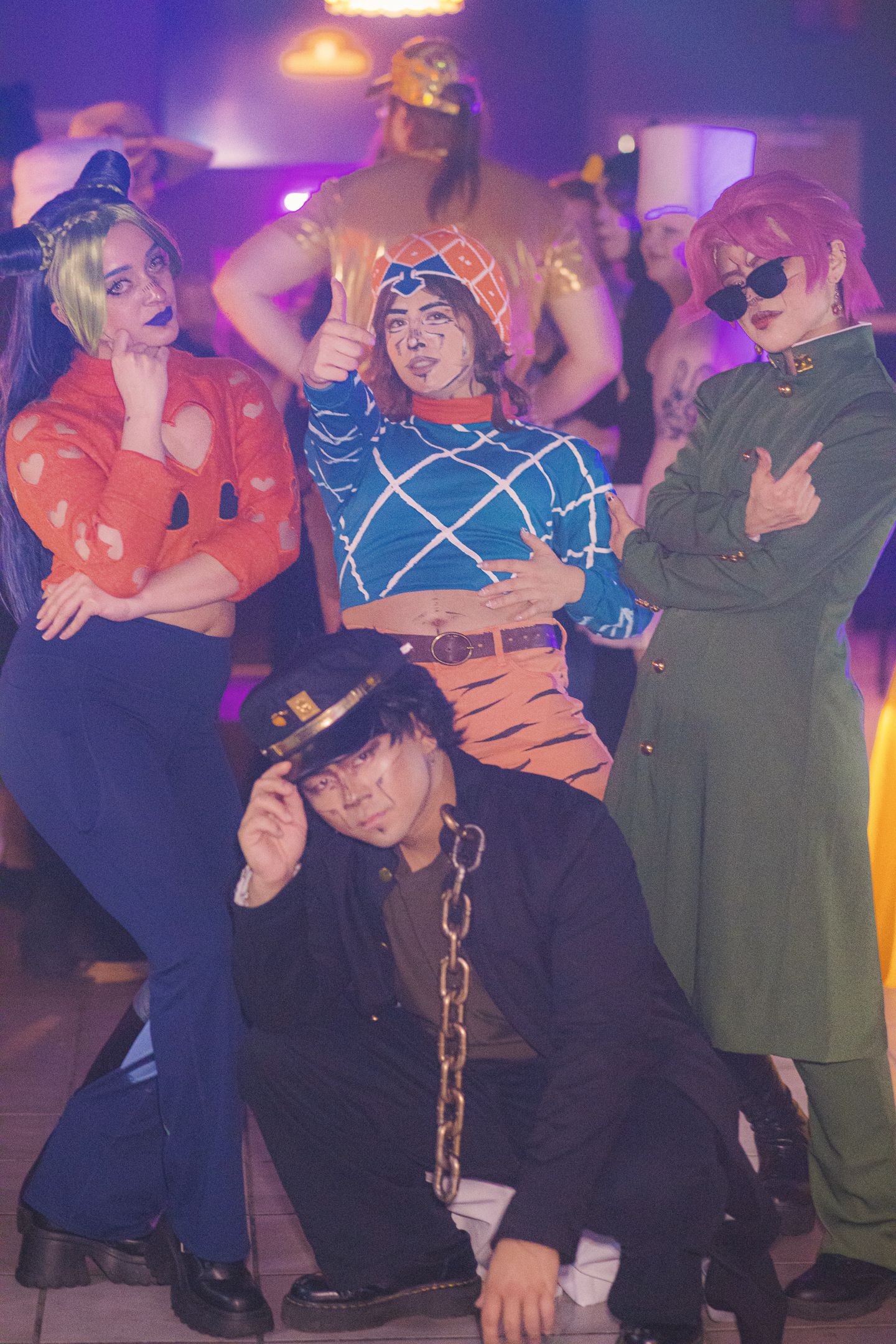 Group of cosplayers posing in colorful costumes at a party event under purple lights.
