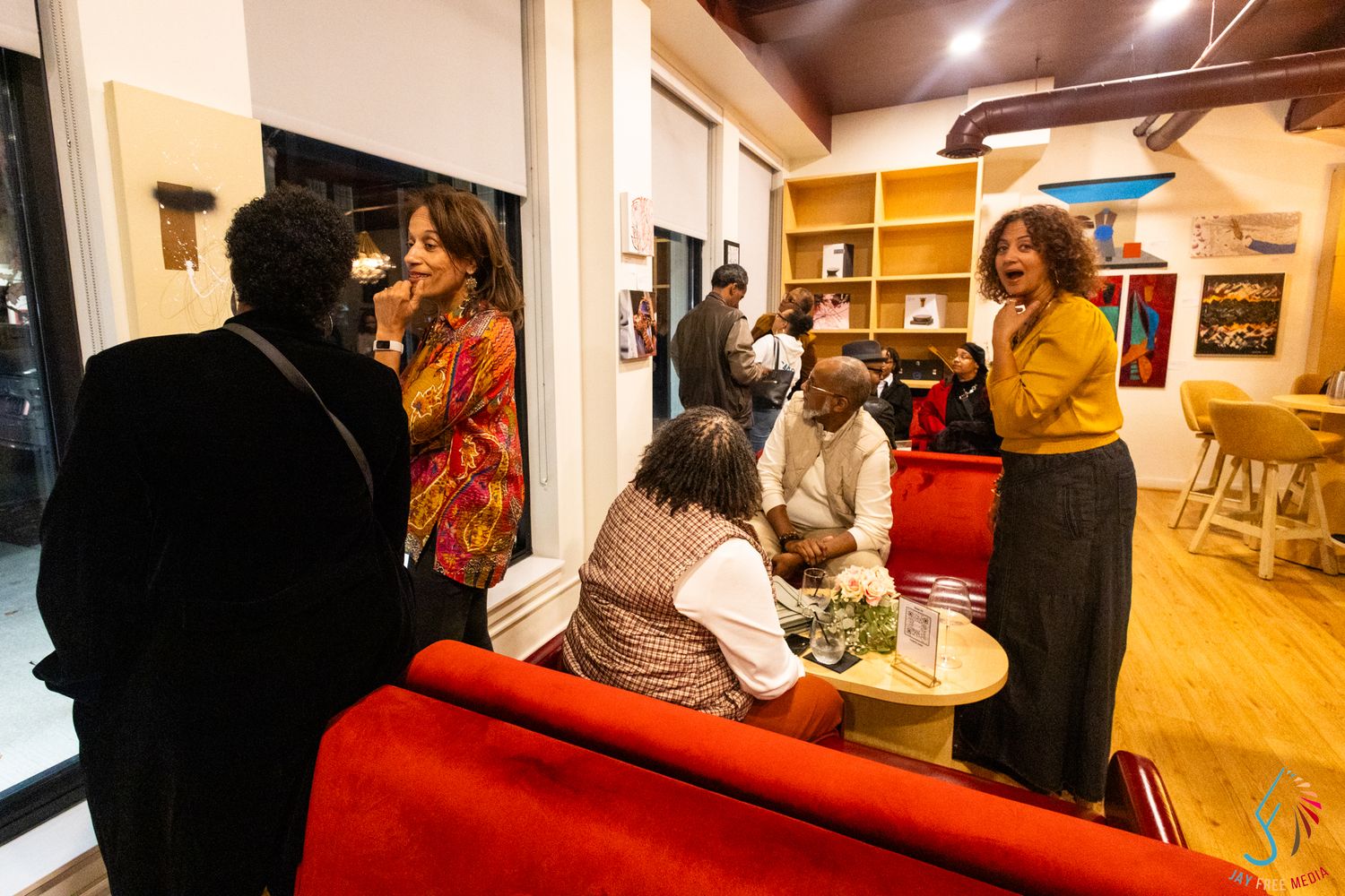 Guests mingle and converse in a stylish art gallery lounge with red sofas.