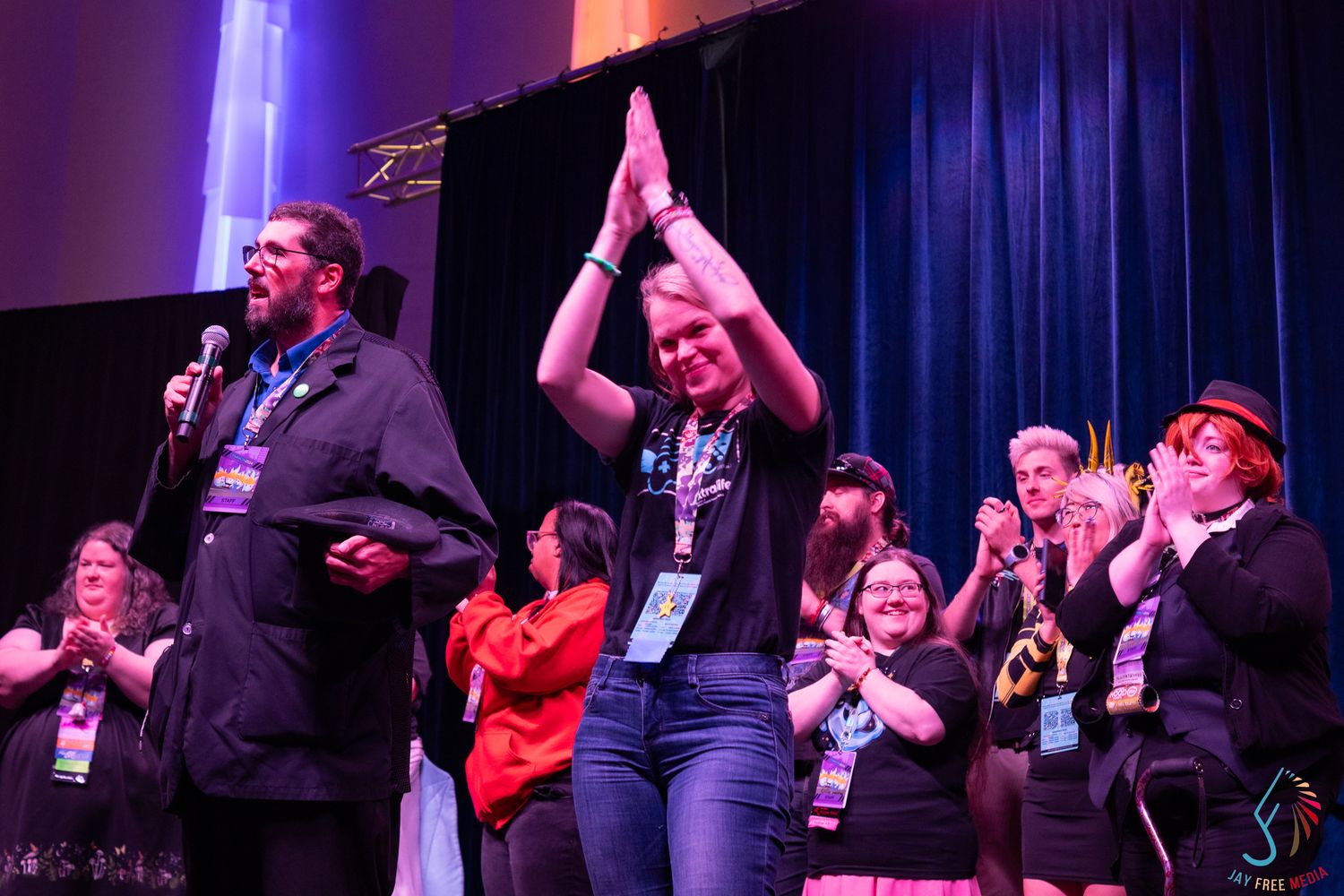 Excited convention attendees celebrate on stage with applause under colorful spotlight lighting.