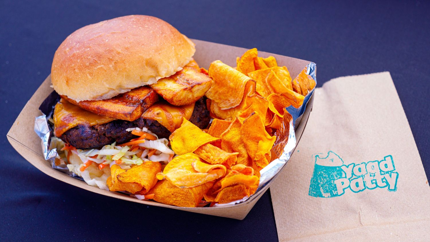 Yard Patty burger with crispy chips in a foil tray, featuring a toasted bun and colorful toppings.