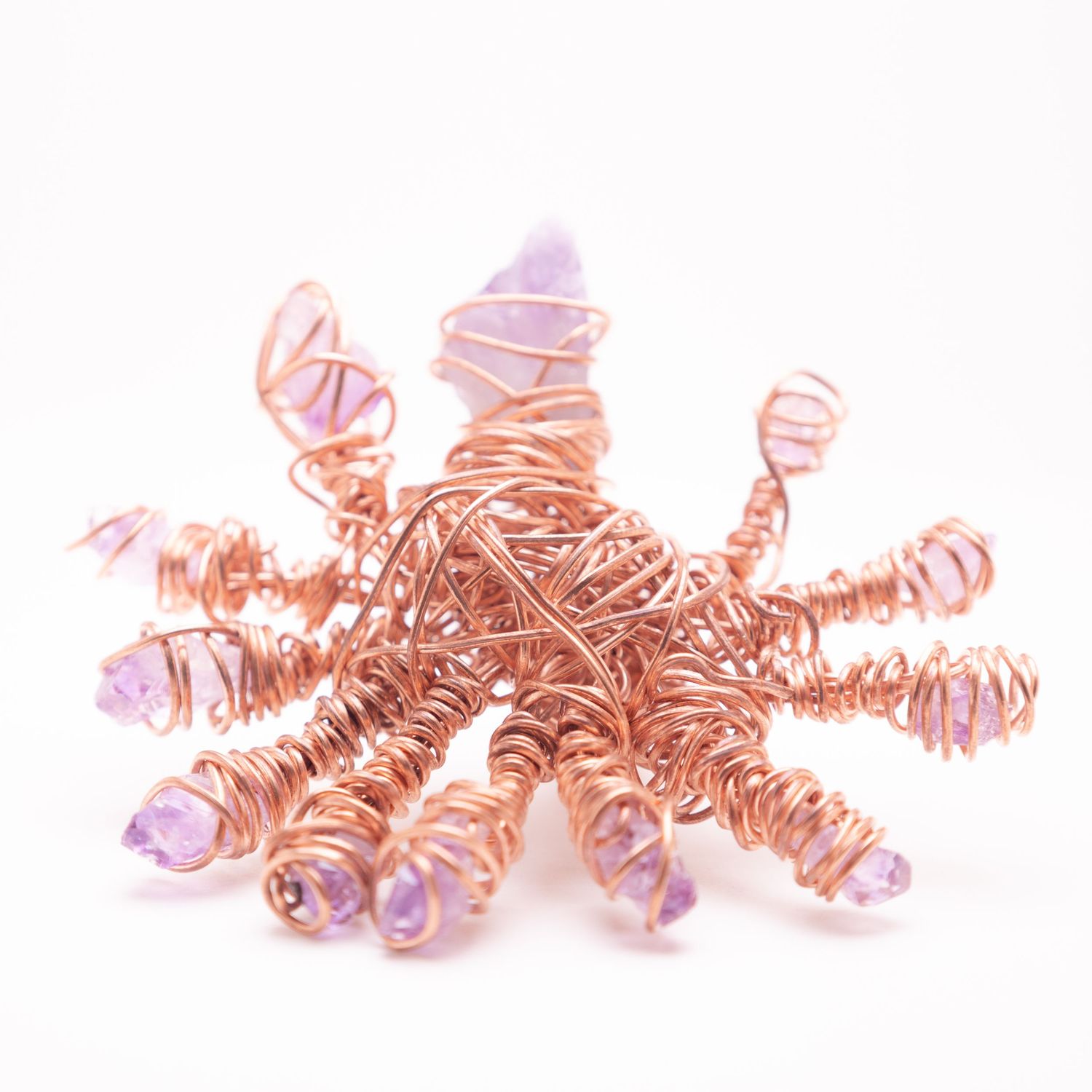 Handmade copper wire wrapped sculpture with purple amethyst crystal chips forming a star or sun shape on white background.