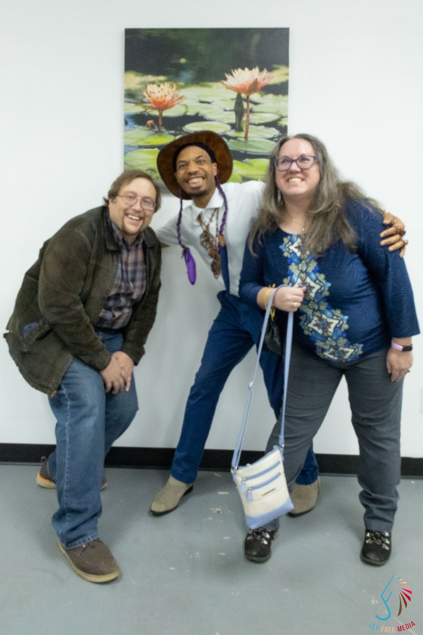 Three people posing happily in front of water lily painting at art show.