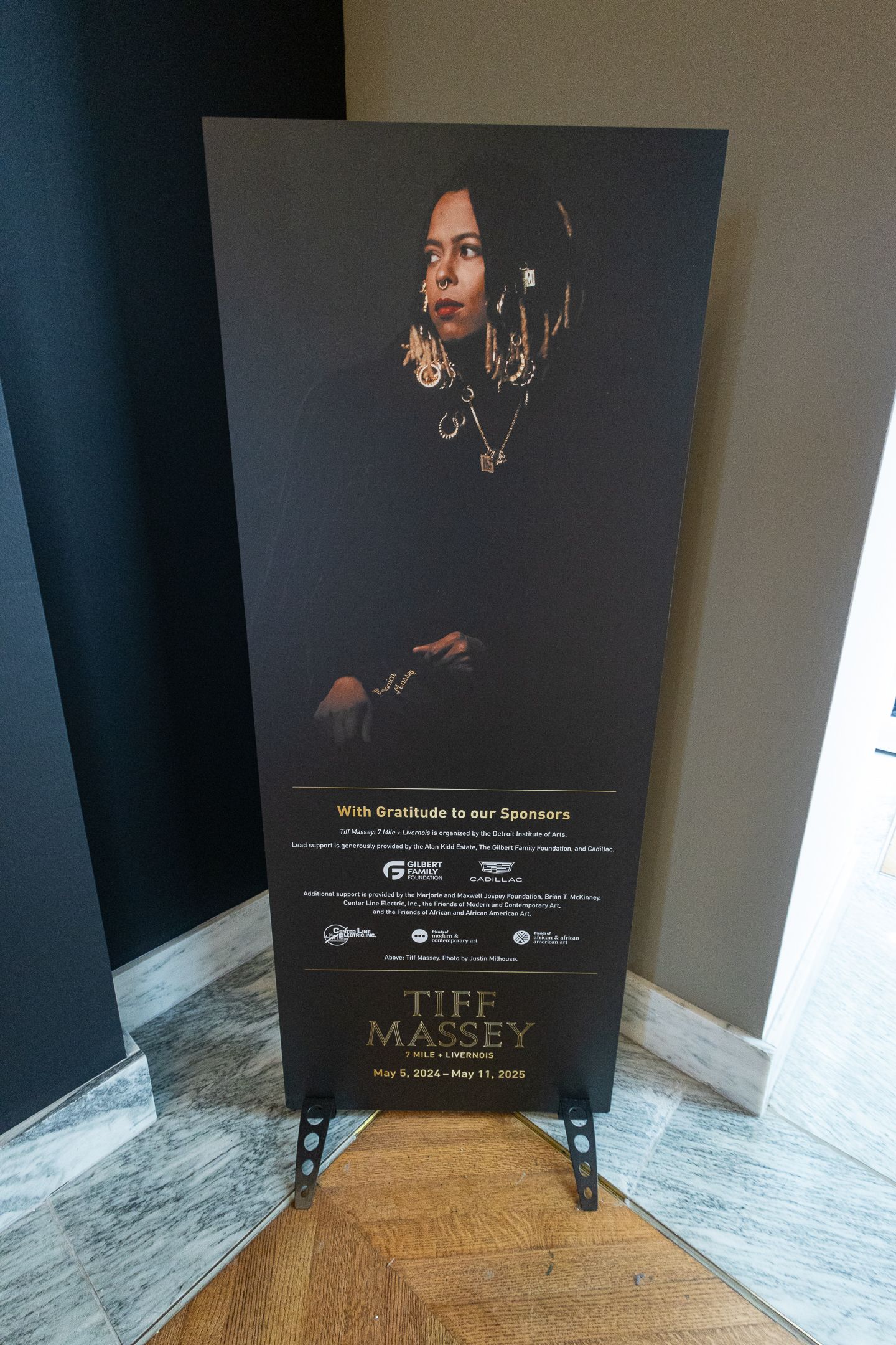 Tiff Massey exhibition sponsor banner featuring a portrait of the Detroit-born jewelry artist at a museum gallery entrance.