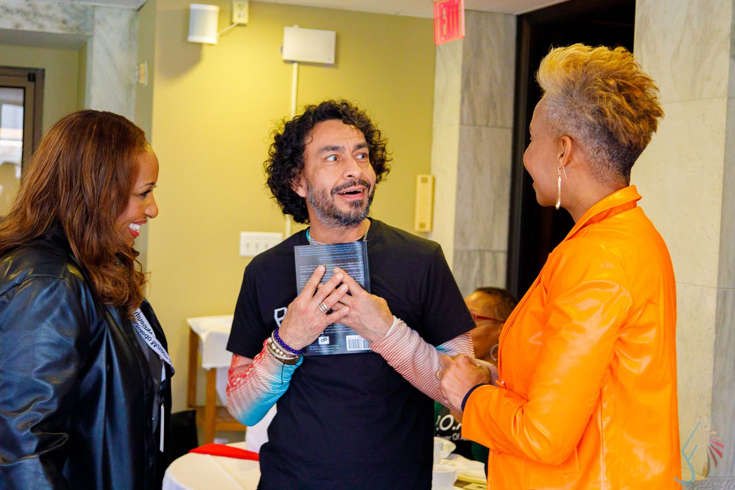 Three people engaged in lively conversation indoors at a social gathering or art event.