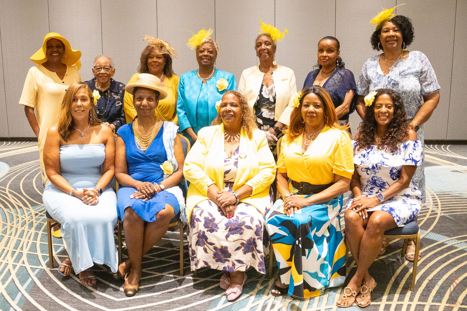 Group of women posing for a formal photo at a banquet event, wearing elegant yellow and blue outfits.