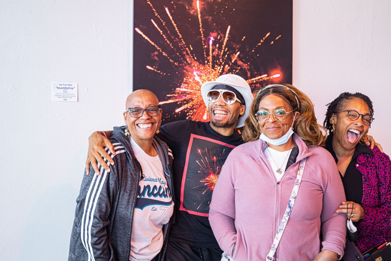 Four people smiling and posing together in front of a fireworks photo at an indoor art gallery event.