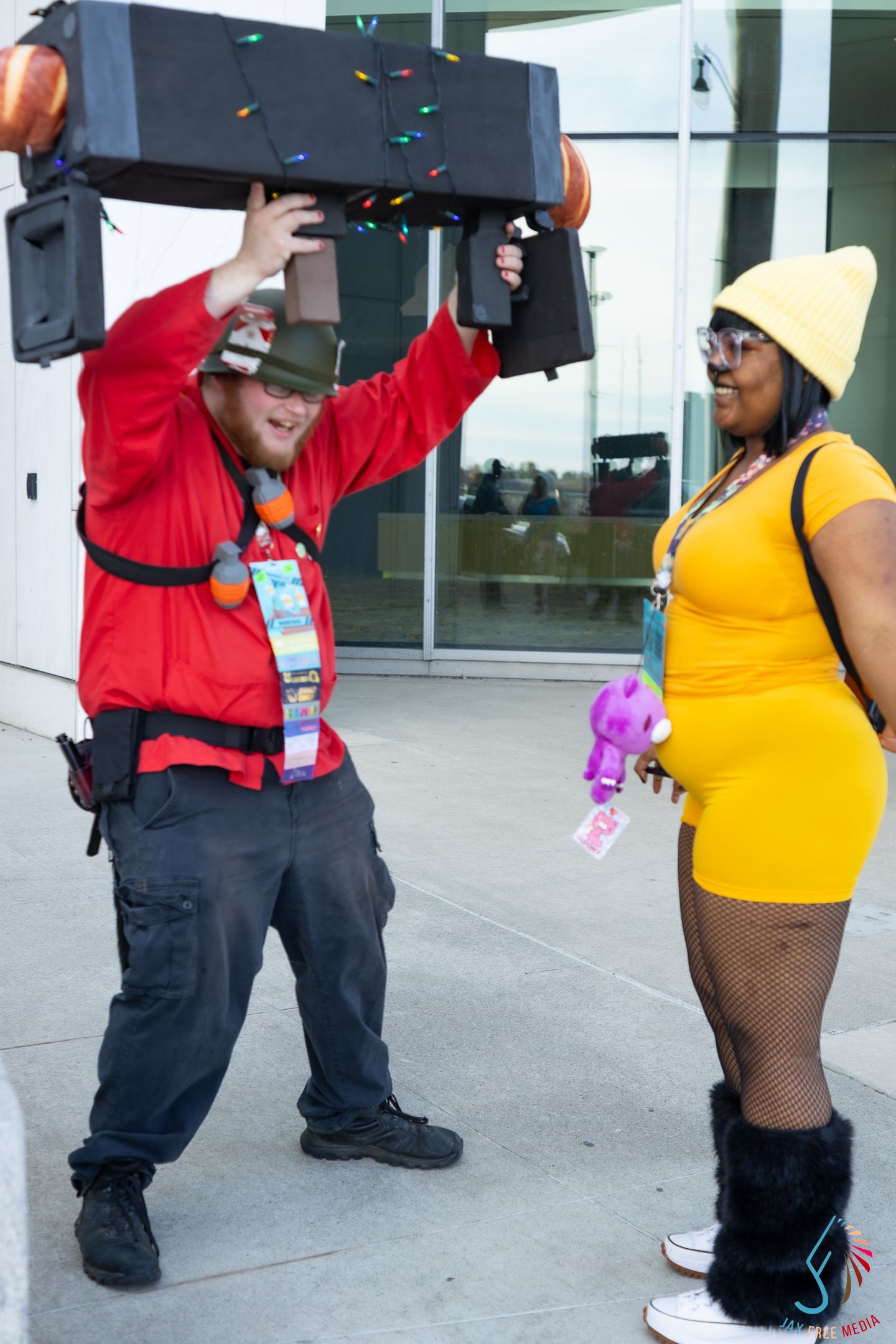 Two cosplayers outside a convention, one in red holding a decorated box overhead.