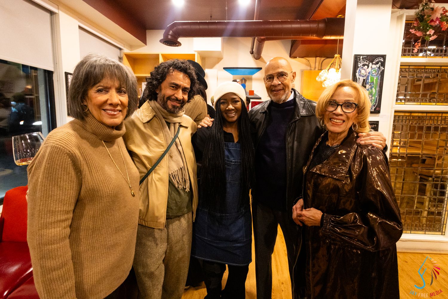 Five people smile together for a group photo at an indoor social gathering event.
