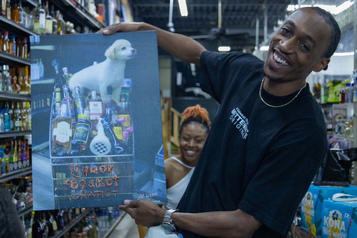 Man holding up a poster in a store, smiling, with a woman seated behind him.