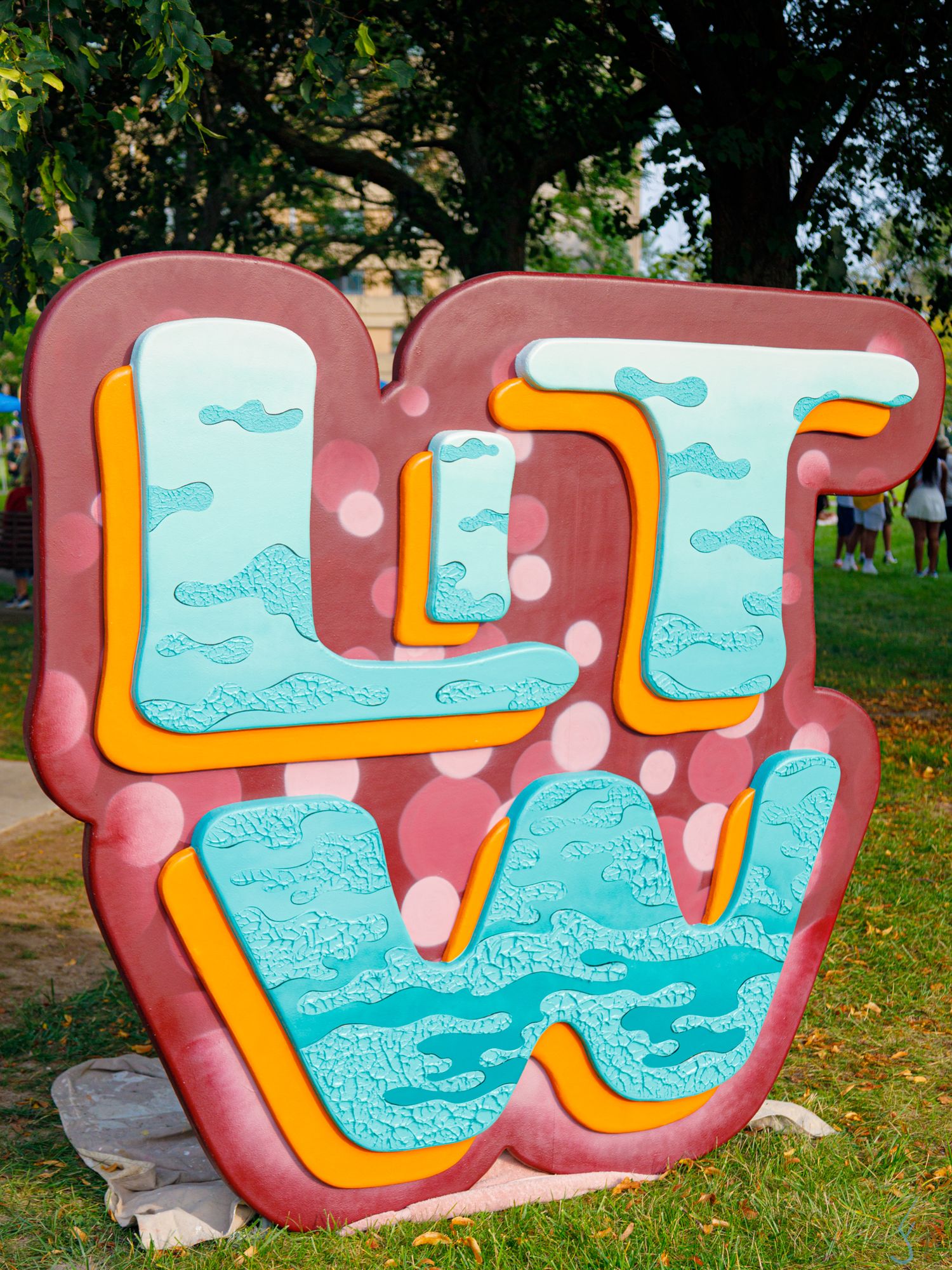Colorful graffiti-style sculpture with teal, pink, and yellow letters displayed outdoors at a festival.