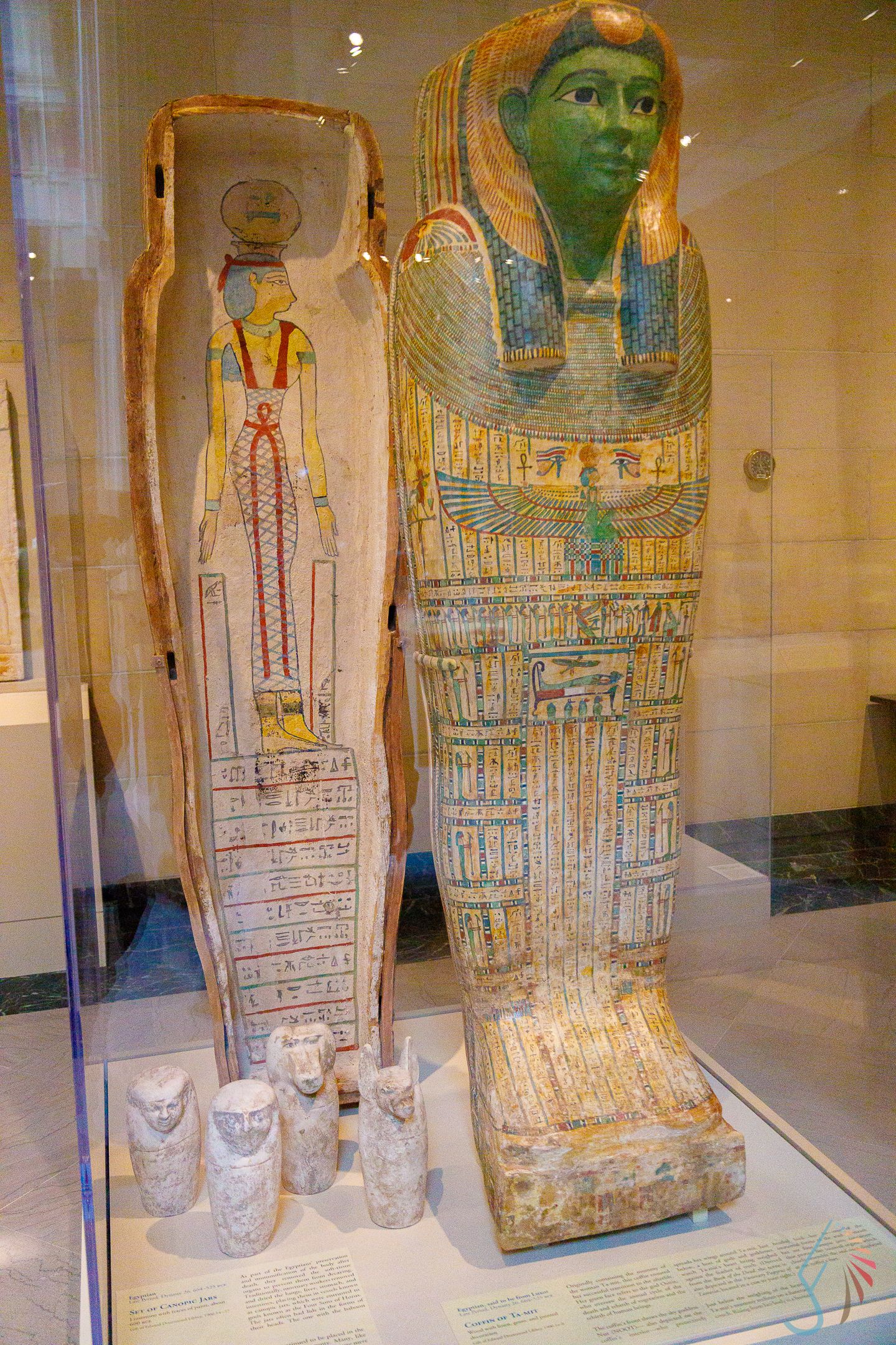 Ancient Egyptian sarcophagus with green face and canopic jars displayed in glass museum case.