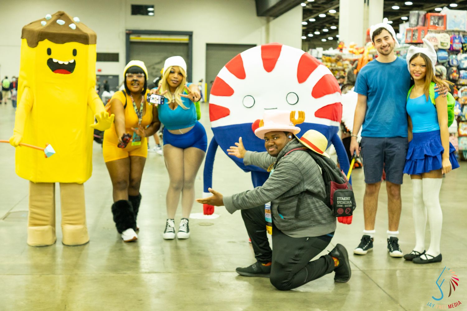 Group of Adventure Time cosplayers posing together at a comic convention on a large expo floor.