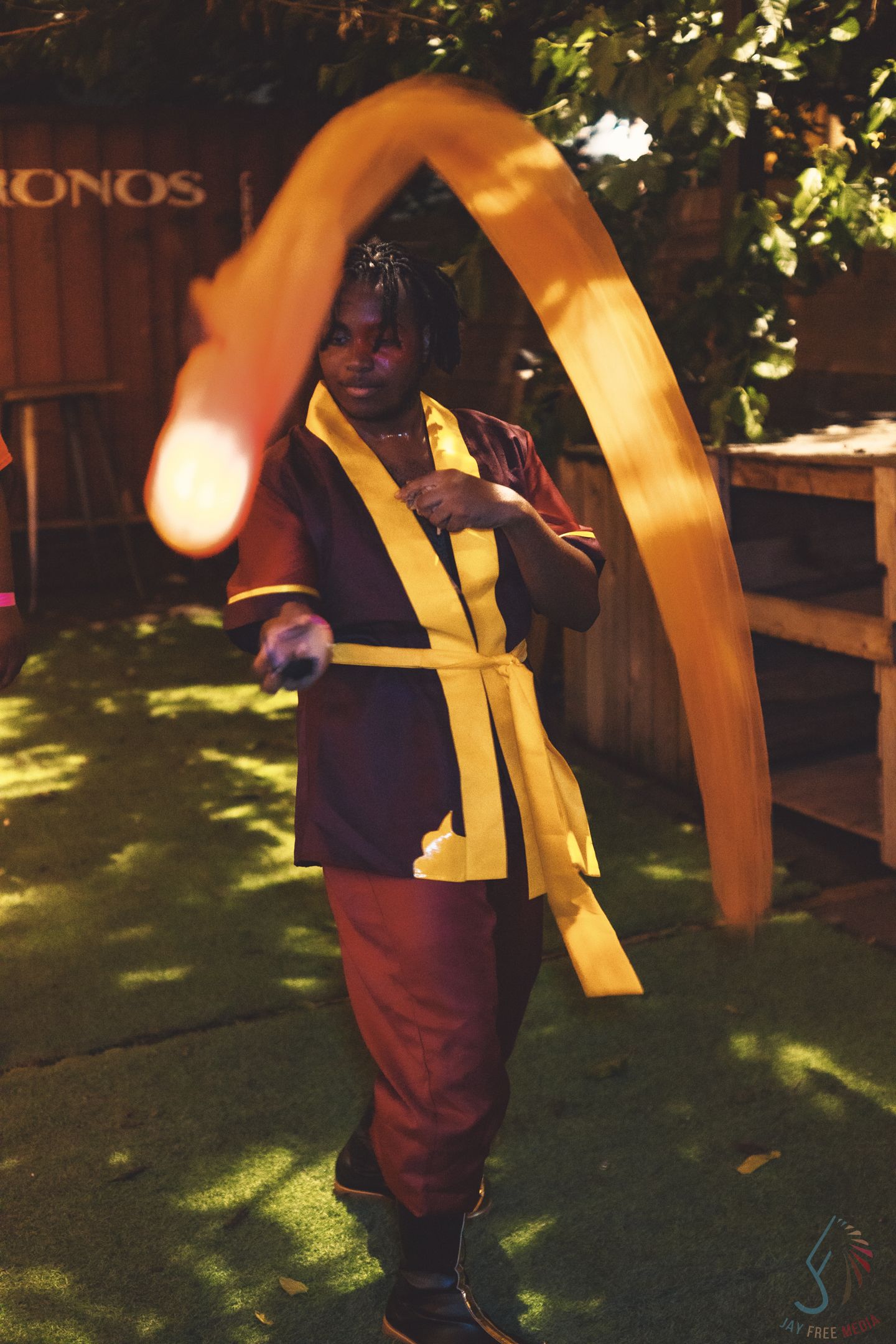 Cosplayer in maroon and yellow outfit spins a large golden boomerang prop outdoors at a cosplay event.