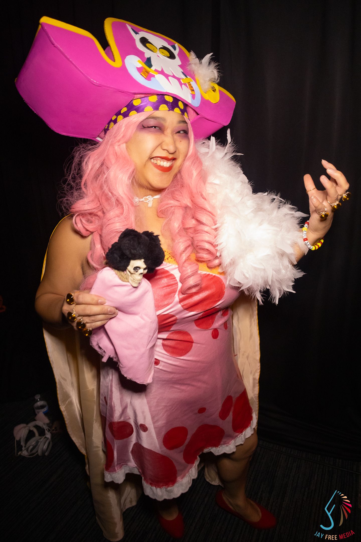 Woman in pink wig and pirate hat cosplay holding a doll at a convention.