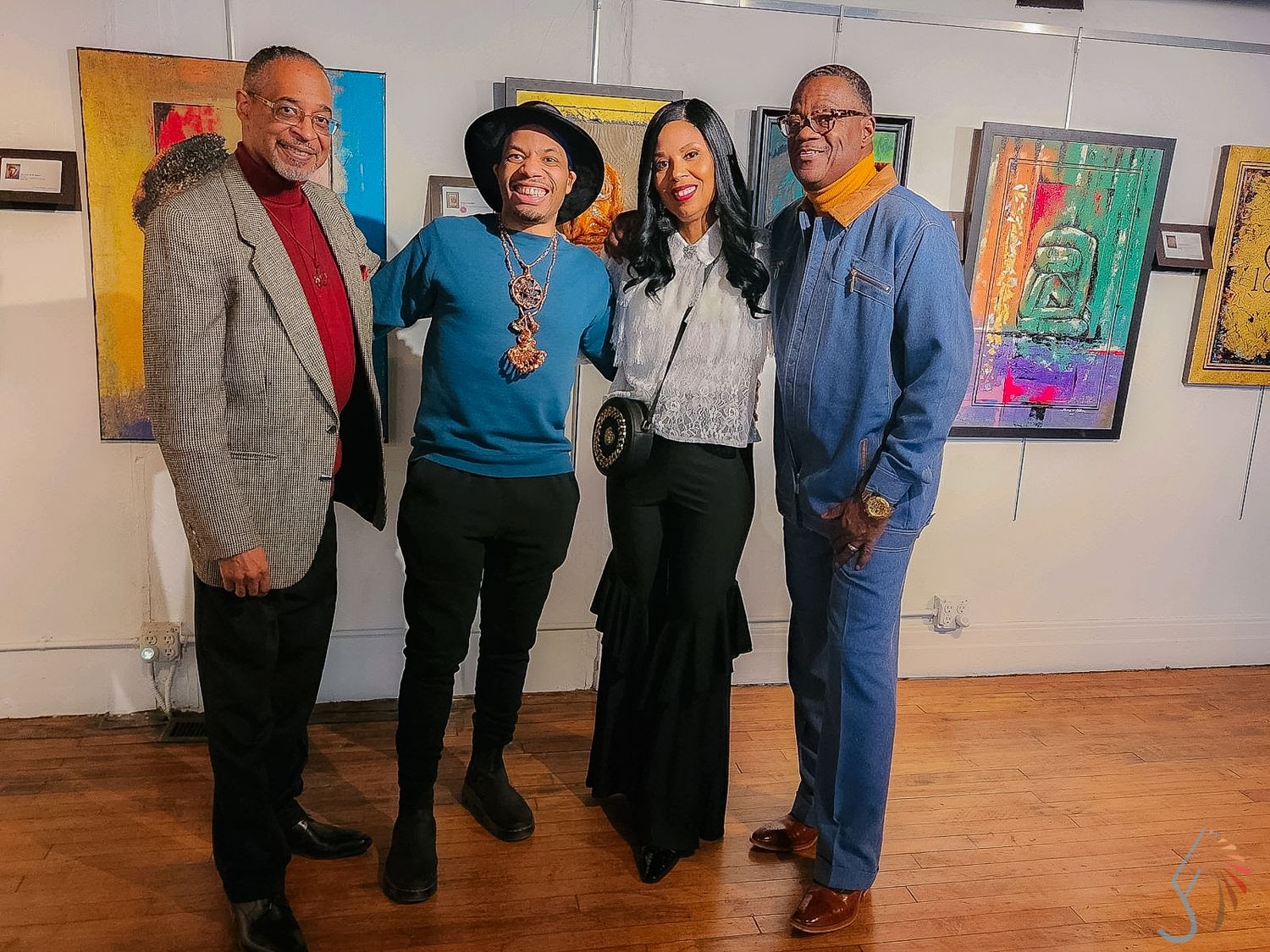 Four people posing together smiling at an art gallery with colorful paintings displayed on the walls behind them.