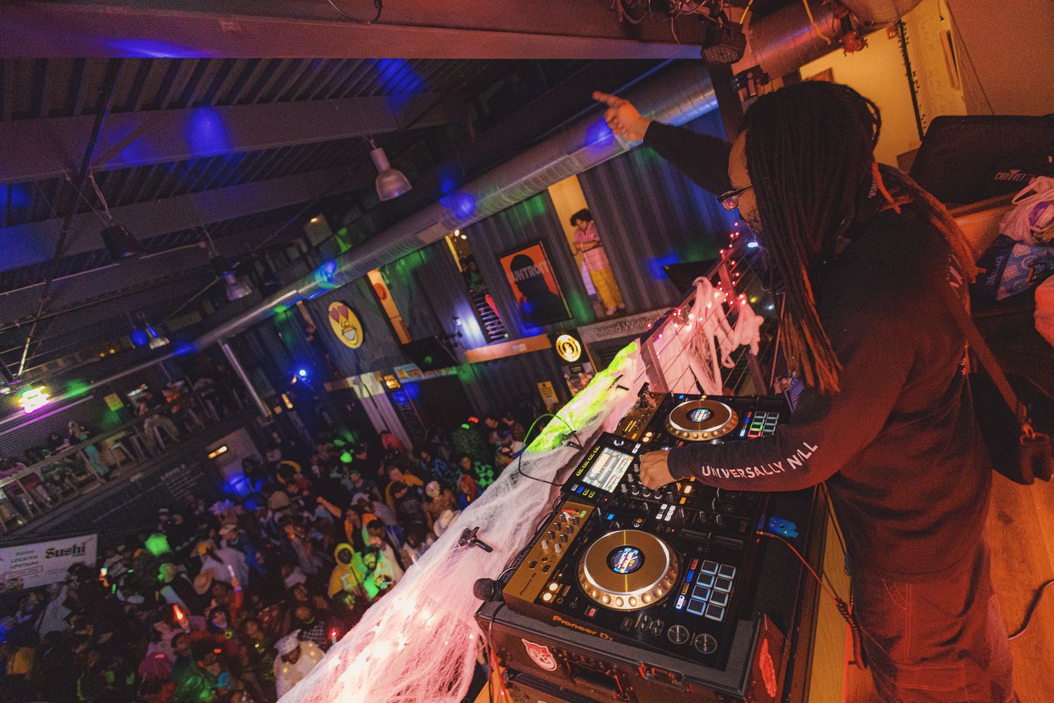 DJ performing at a vibrant nightclub party with colorful lights and a packed dance floor crowd.