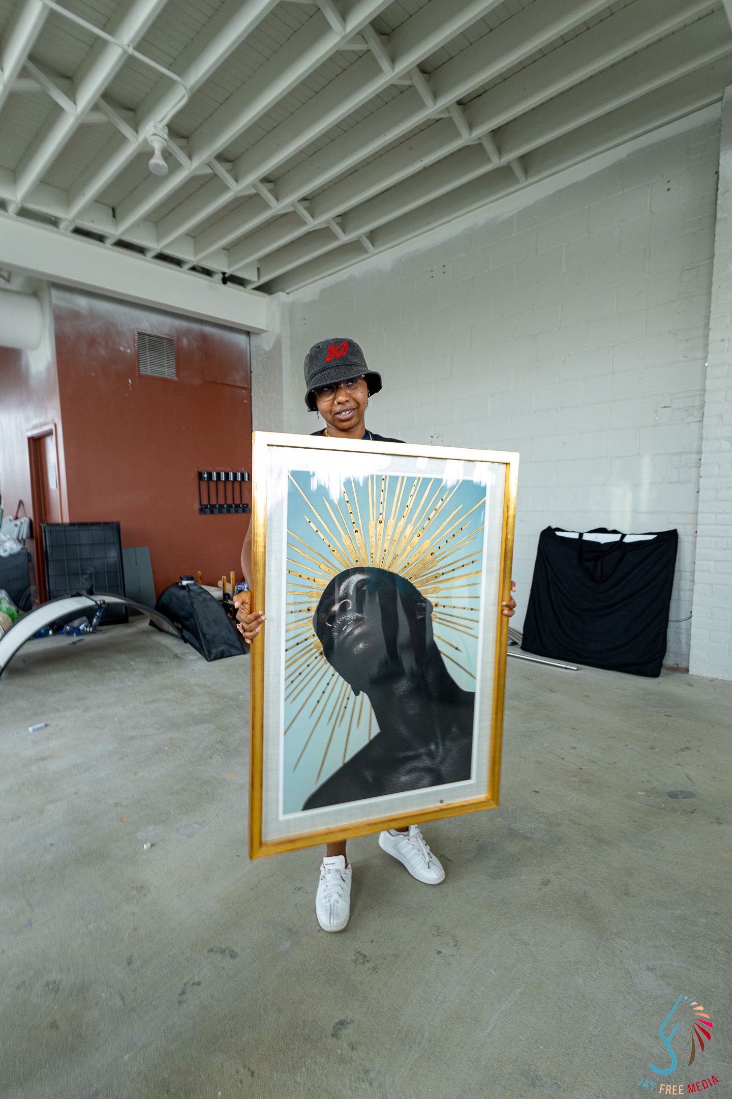 Artist holding a large framed portrait painting with golden halo in an empty warehouse space.