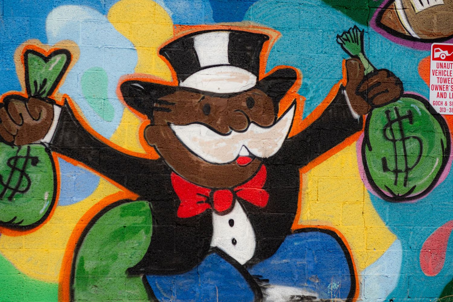 Colorful graffiti mural of Monopoly man holding money bags on a urban wall.