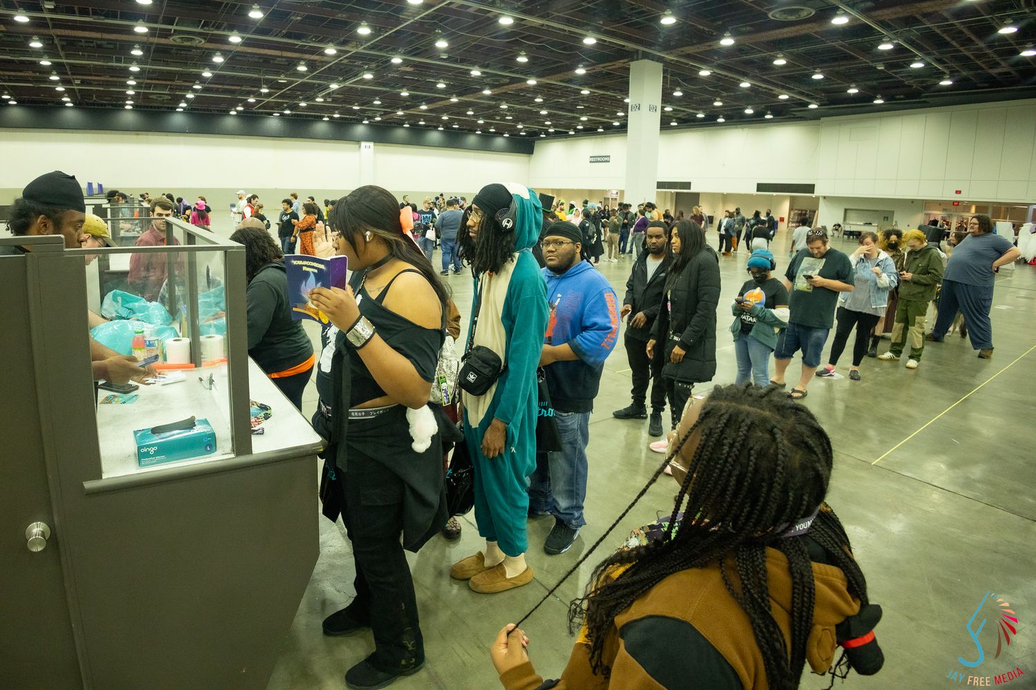 Cosplay convention attendees browse vendor booths inside a large convention hall with diverse crowd in costumes.