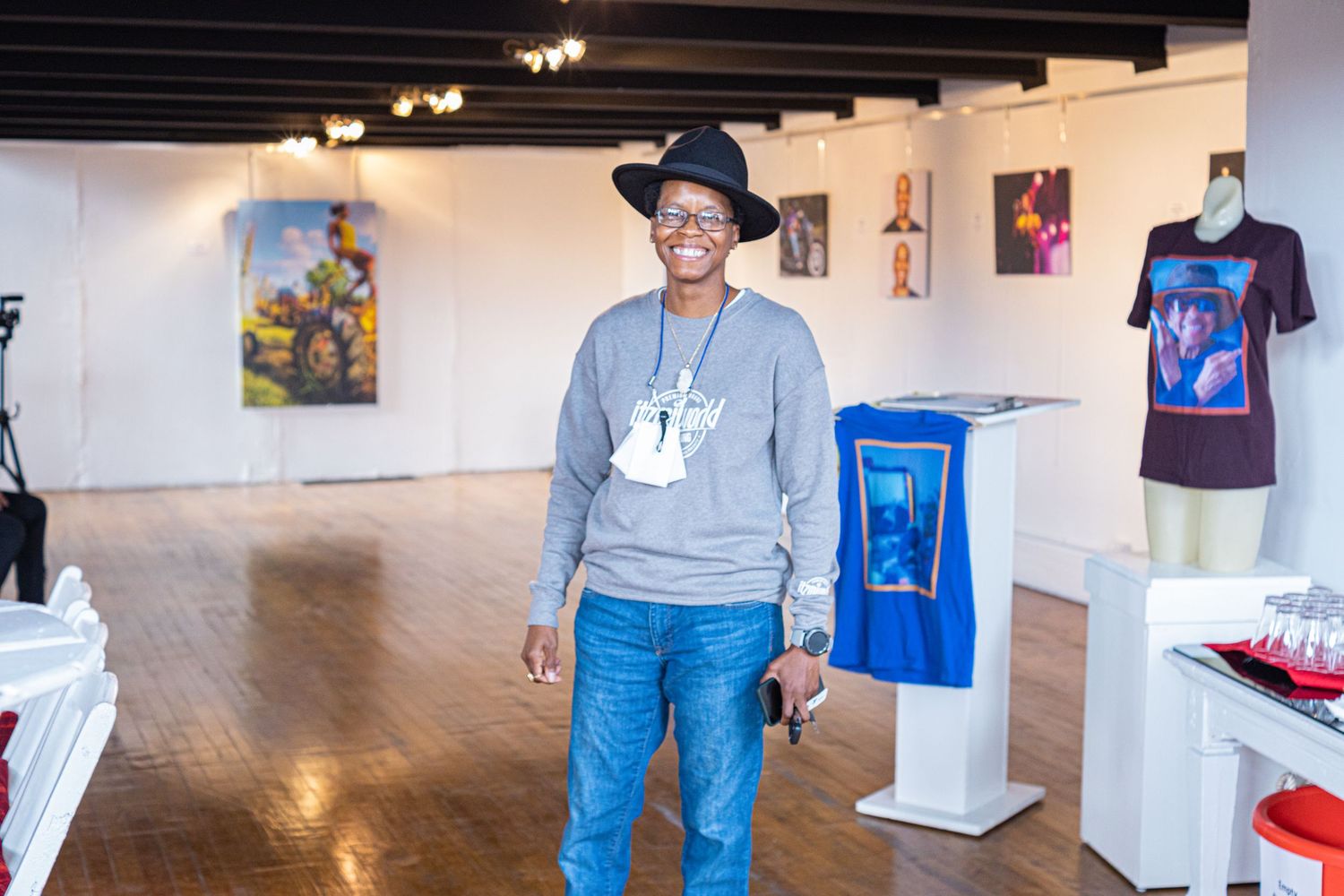 Artist standing in a bright art gallery with colorful paintings and merchandise displays on wooden floors.