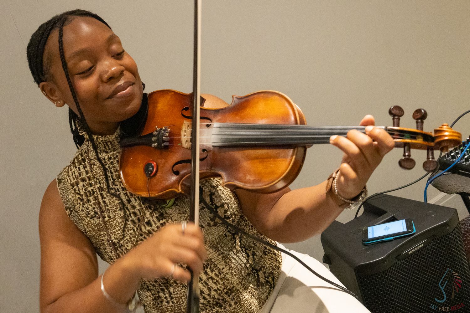 Young woman playing violin, performing with a wooden instrument, wearing a sleeveless patterned top in a modern venue.