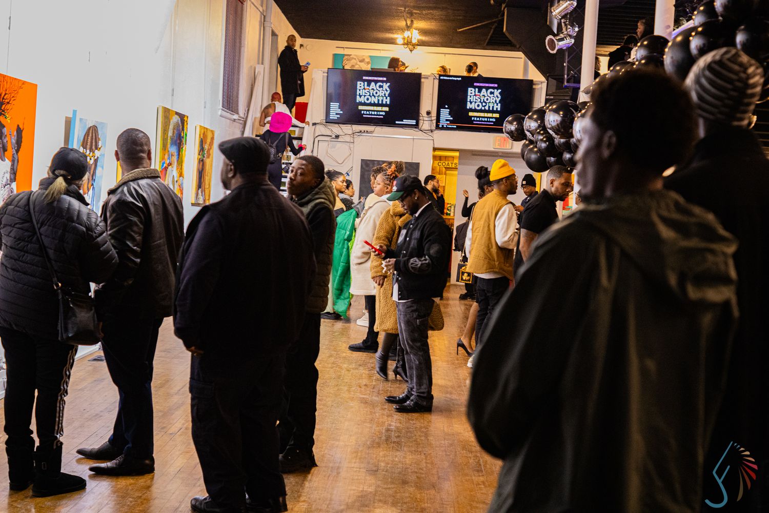 Crowd of people attending a Black art gallery exhibition event in a spacious well-lit venue.