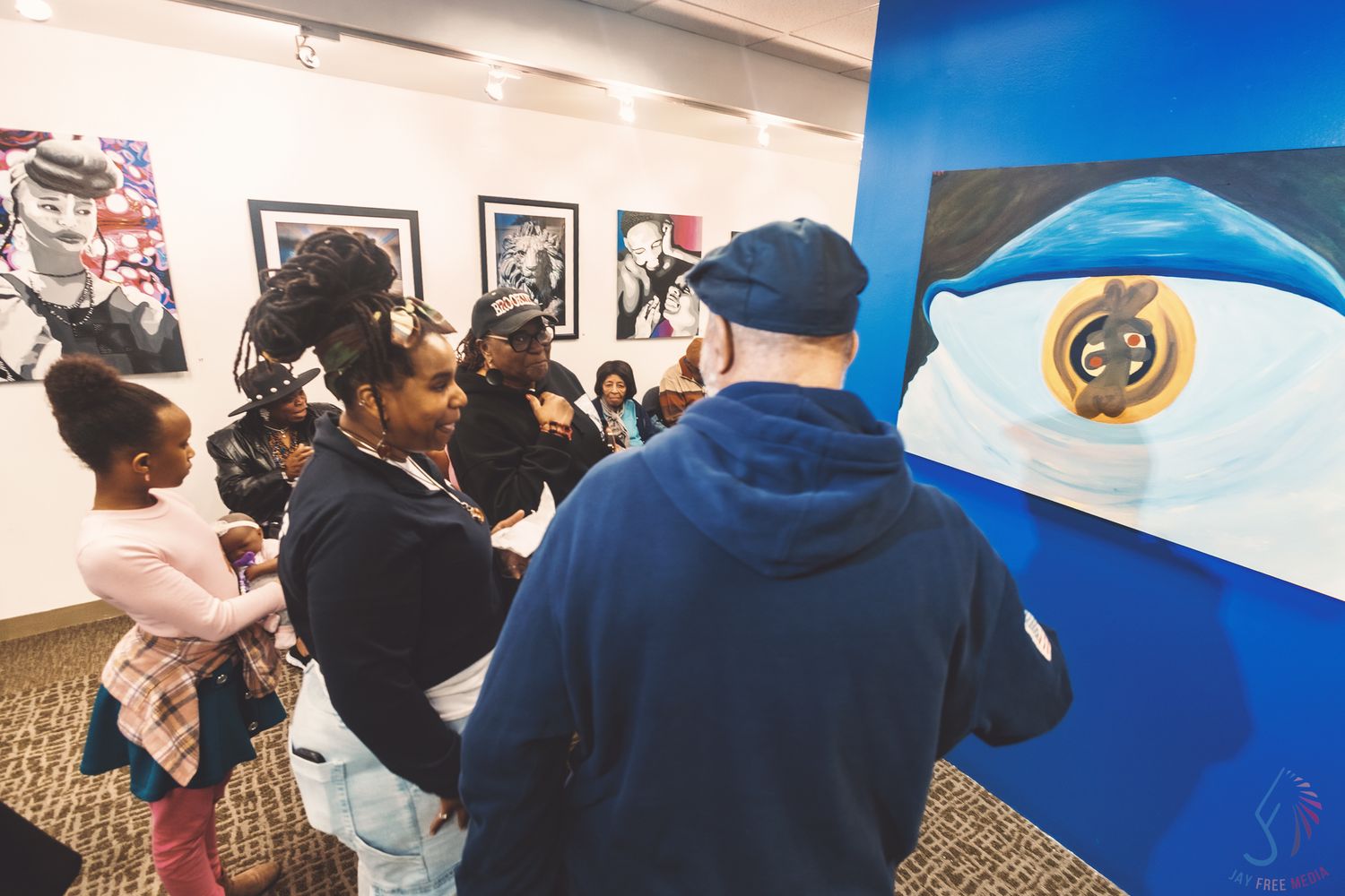 Group of visitors viewing colorful artwork in a gallery, with a large blue painting prominently displayed on the wall.