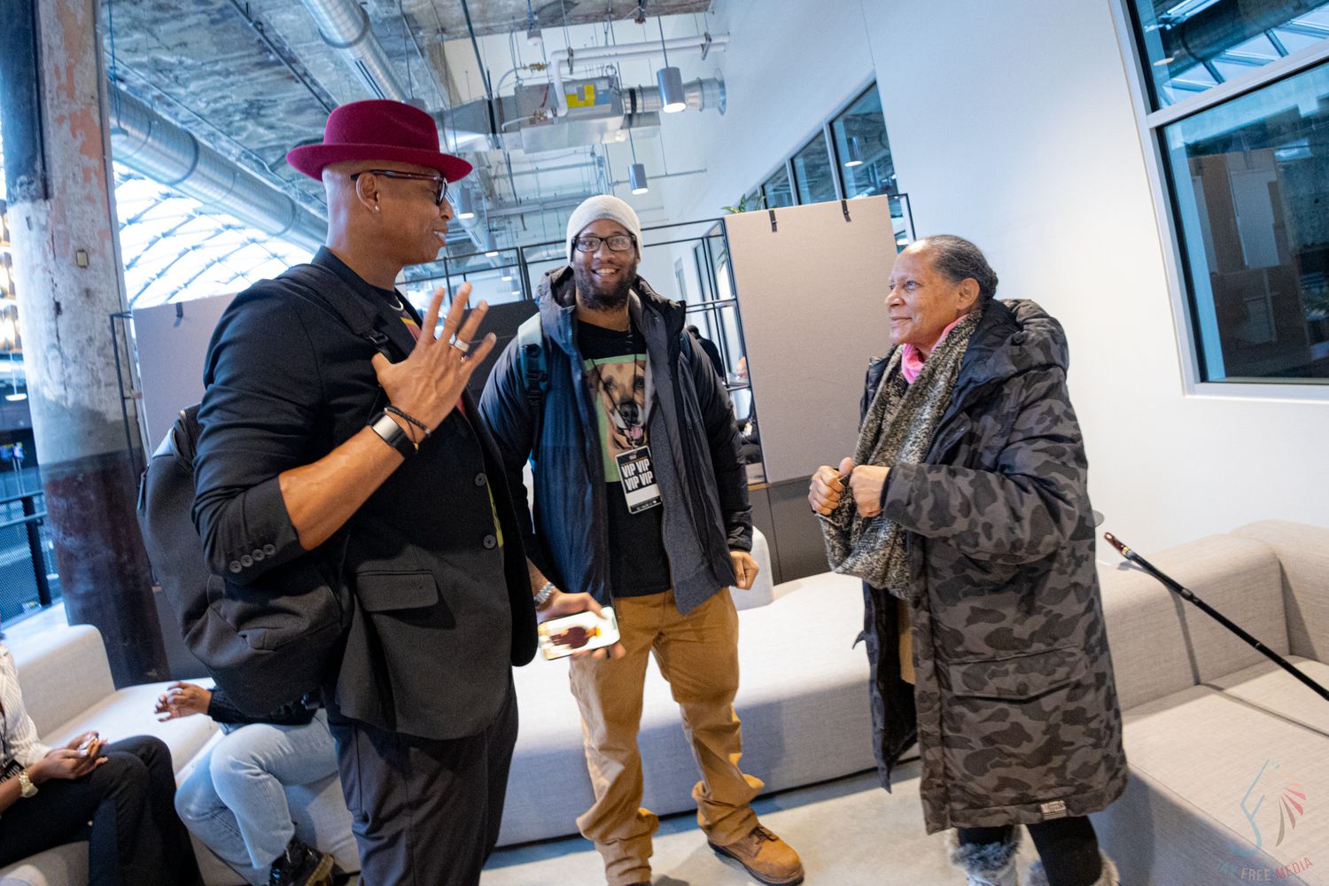 Three people engaged in animated conversation at an indoor networking event in a modern bright space.