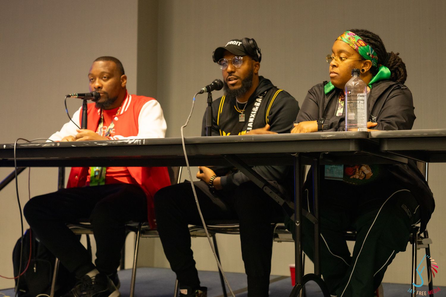Three panelists sit at table with microphones during comic convention discussion panel presentation.