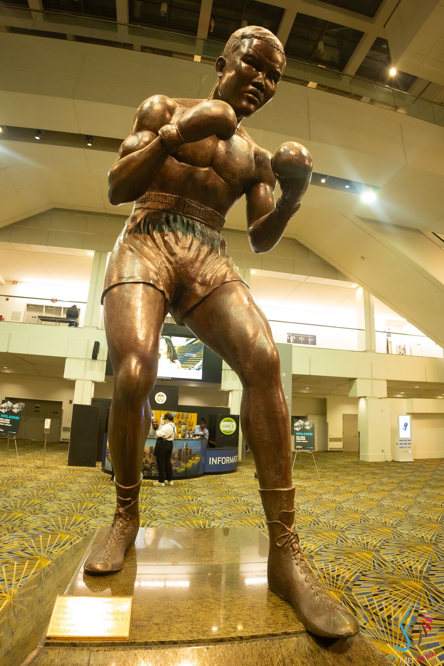 Bronze boxing statue of a fighter in fighting stance displayed in convention center lobby with patterned carpet.