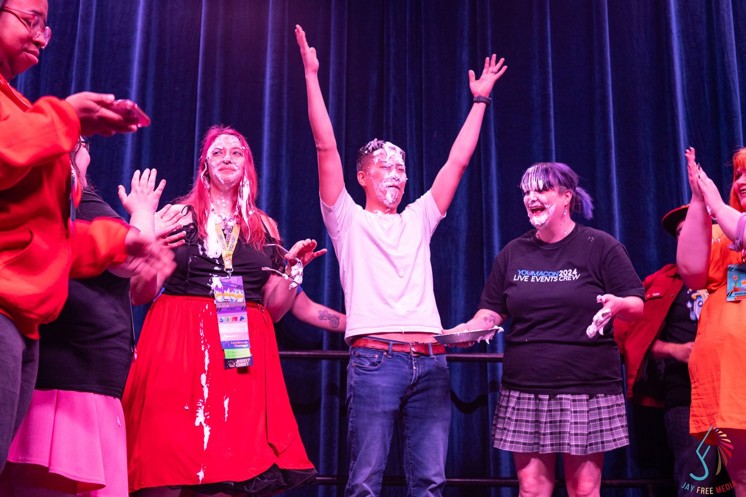 Excited convention attendees celebrate on stage with arms raised under blue stage lighting.