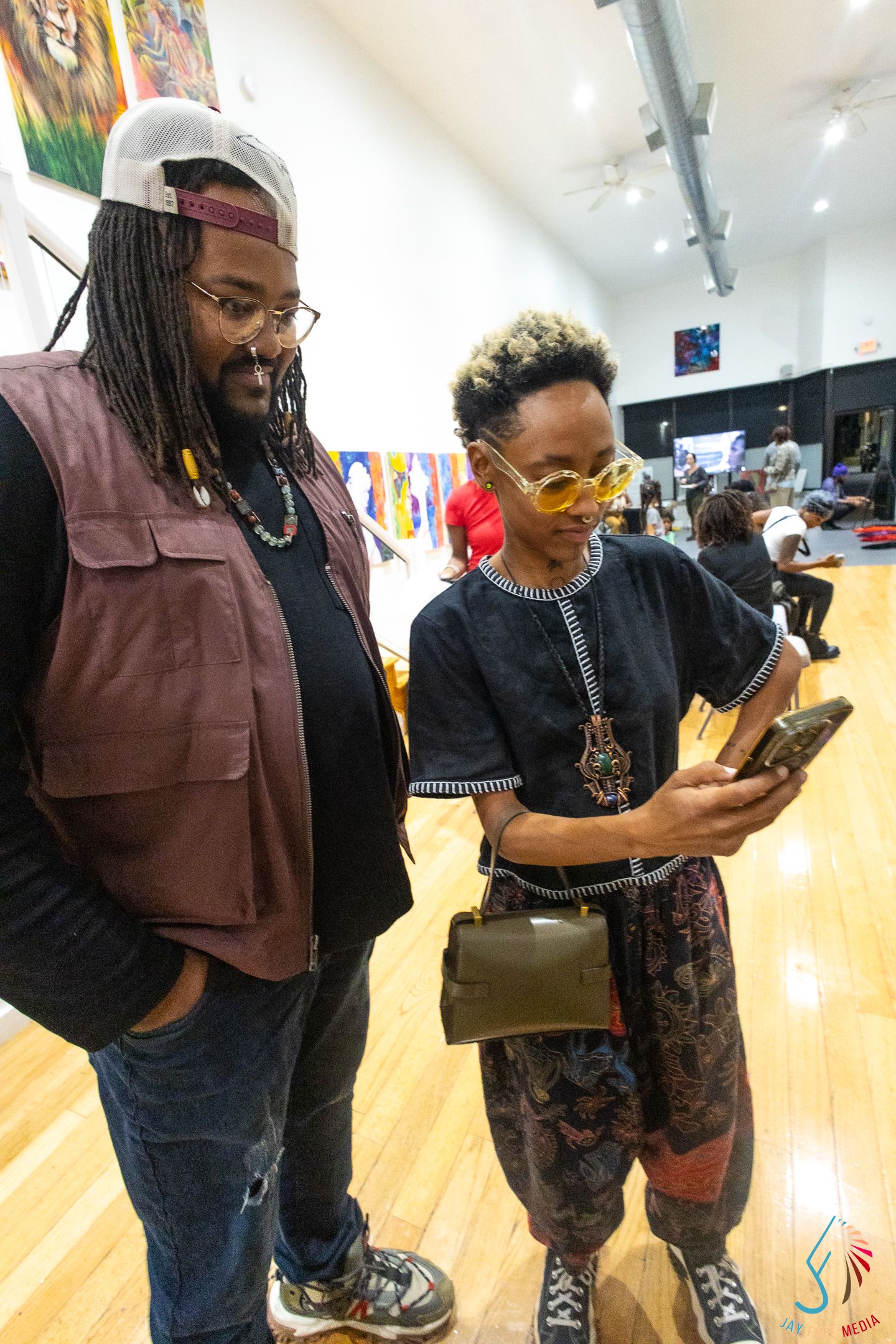 Two stylishly dressed people looking at a smartphone inside an art gallery event space.