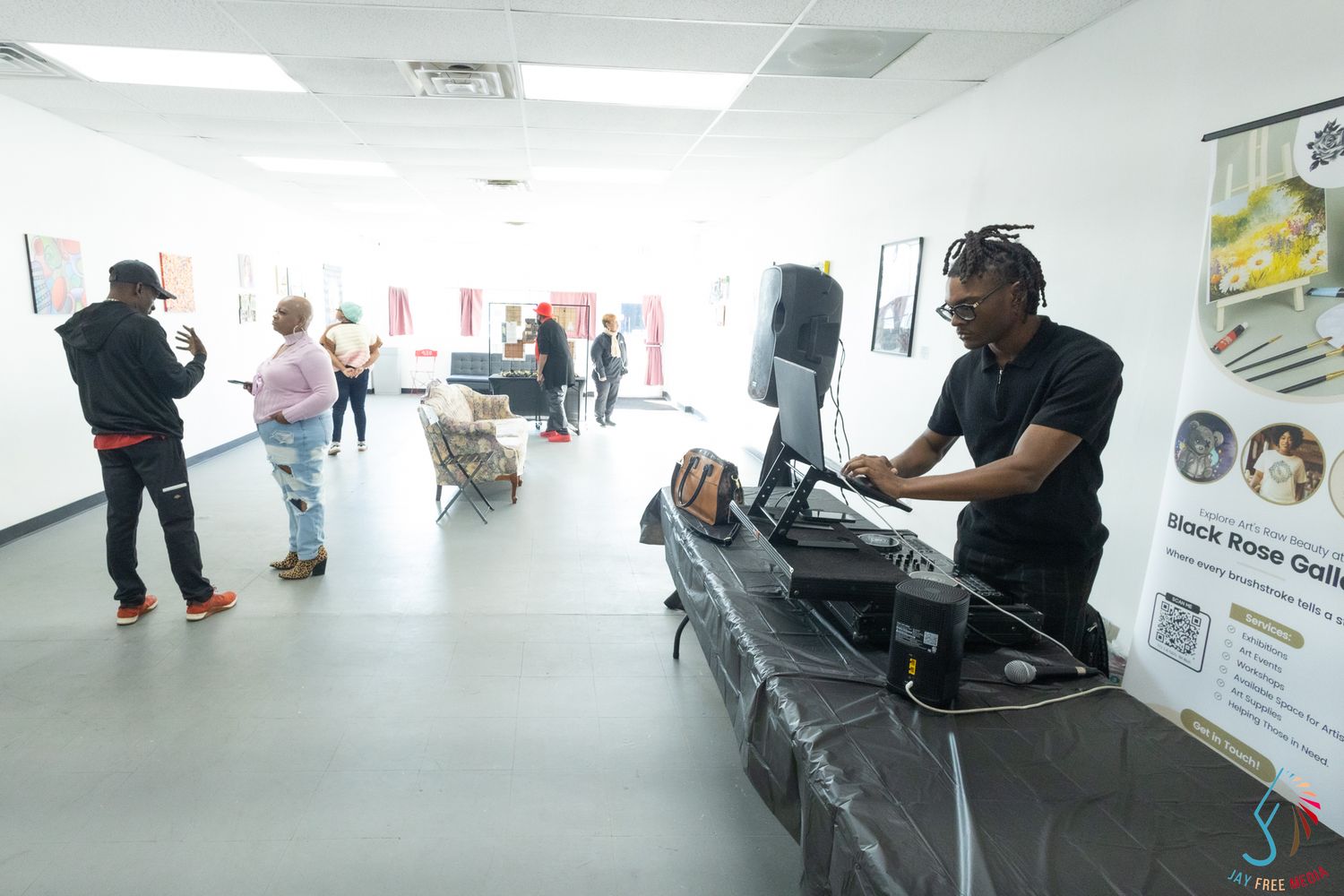 A DJ performs at an indoor event space while guests mingle in the background near artwork displays.