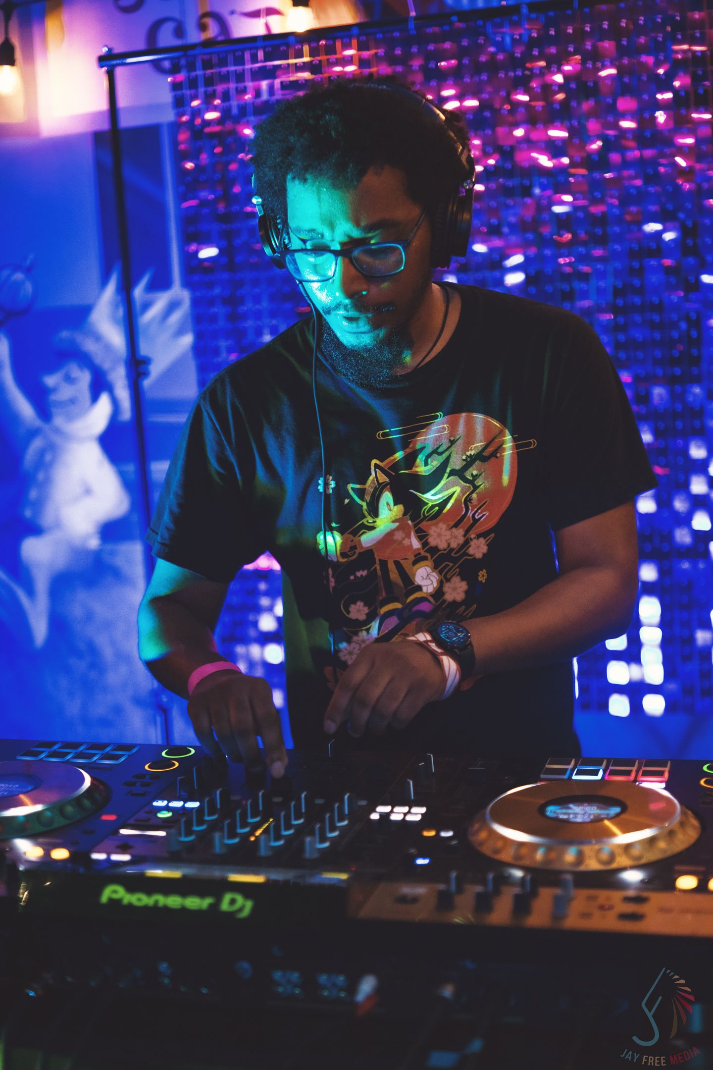 DJ performs at a mixing board under blue and purple stage lighting.
