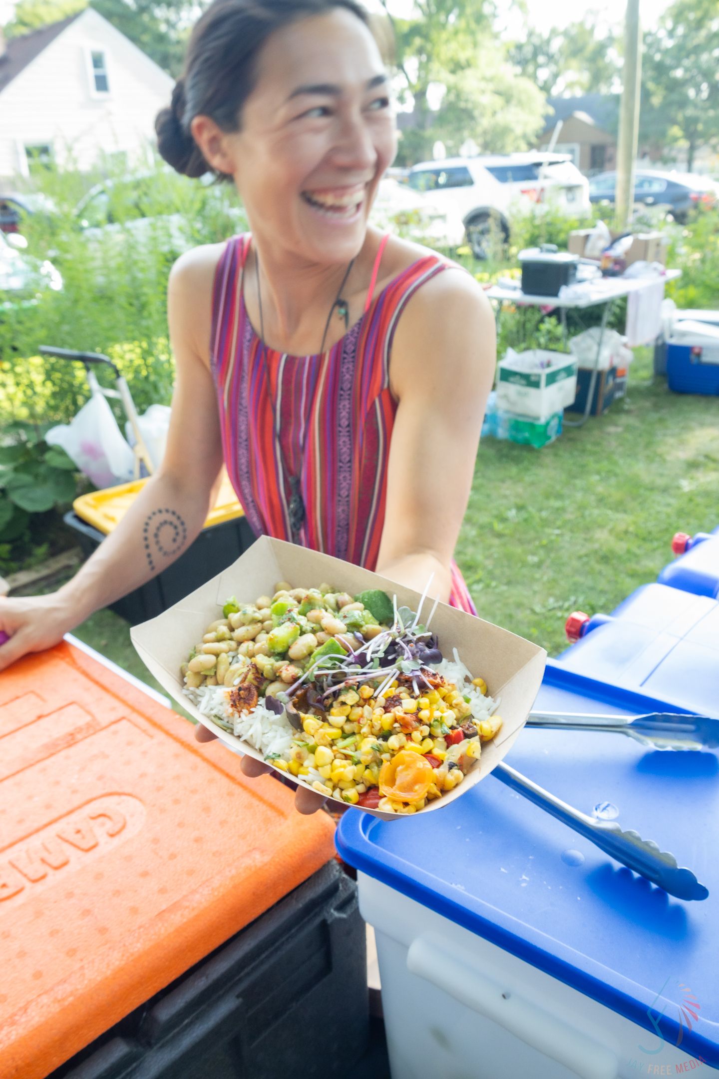 Smiling woman holding colorful fresh salad bowl at outdoor food market event.