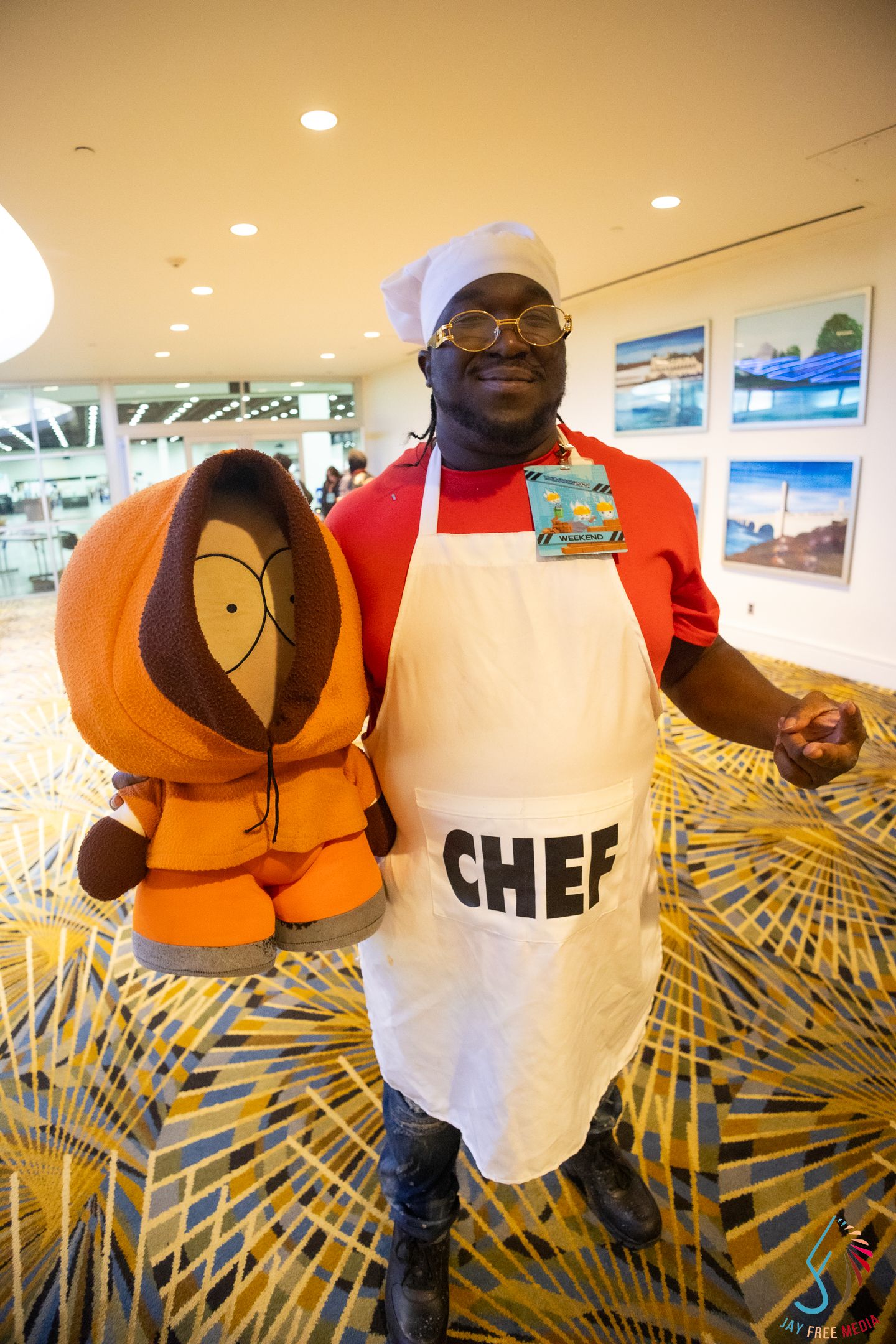 Man cosplaying as Chef from South Park poses with a Kenny plush toy at a convention.