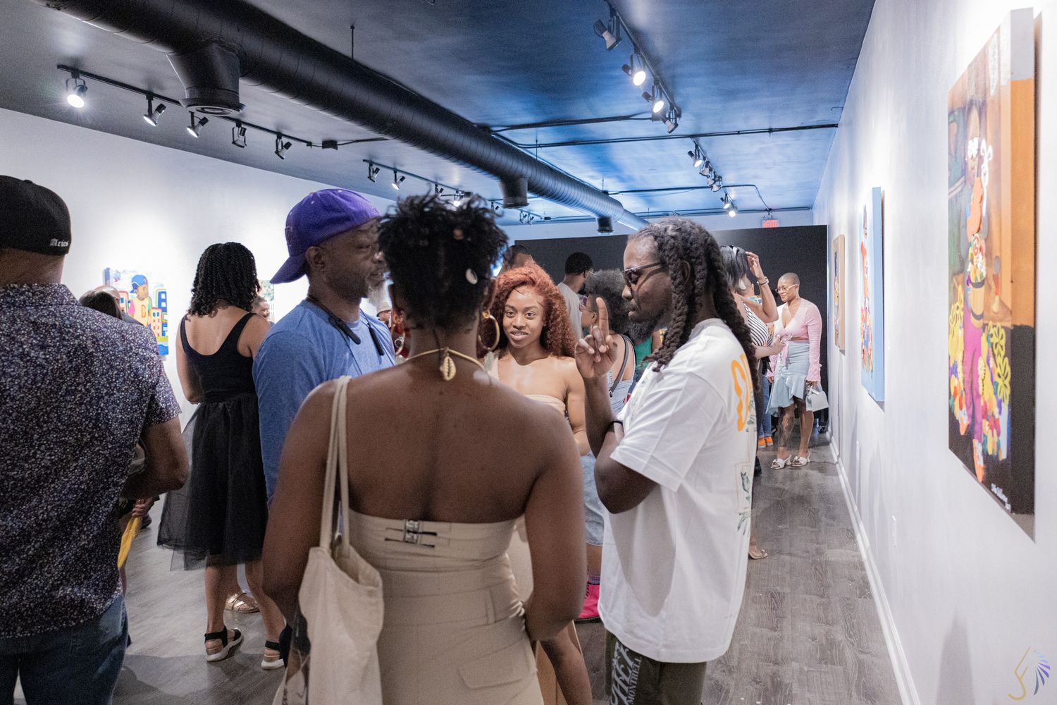Diverse group of art enthusiasts mingling at a contemporary gallery opening with colorful paintings on white walls.