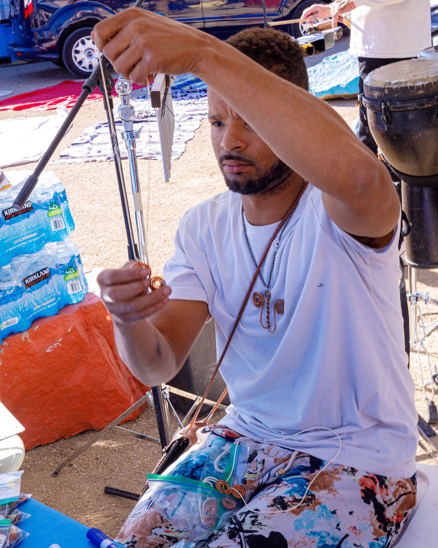 Man in a white t-shirt working with art supplies at an outdoor market stall.