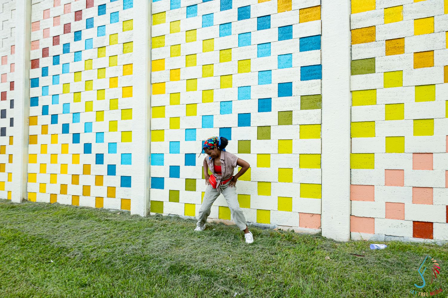 Young Black woman posing against a vibrant colorful grid mural wall on a bright sunny day.