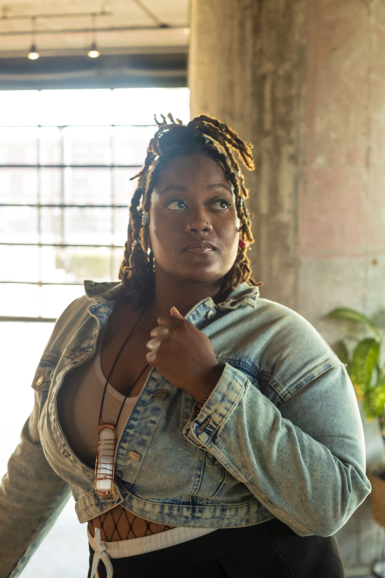 Person wearing denim jacket and hoodie in an industrial-style interior space.