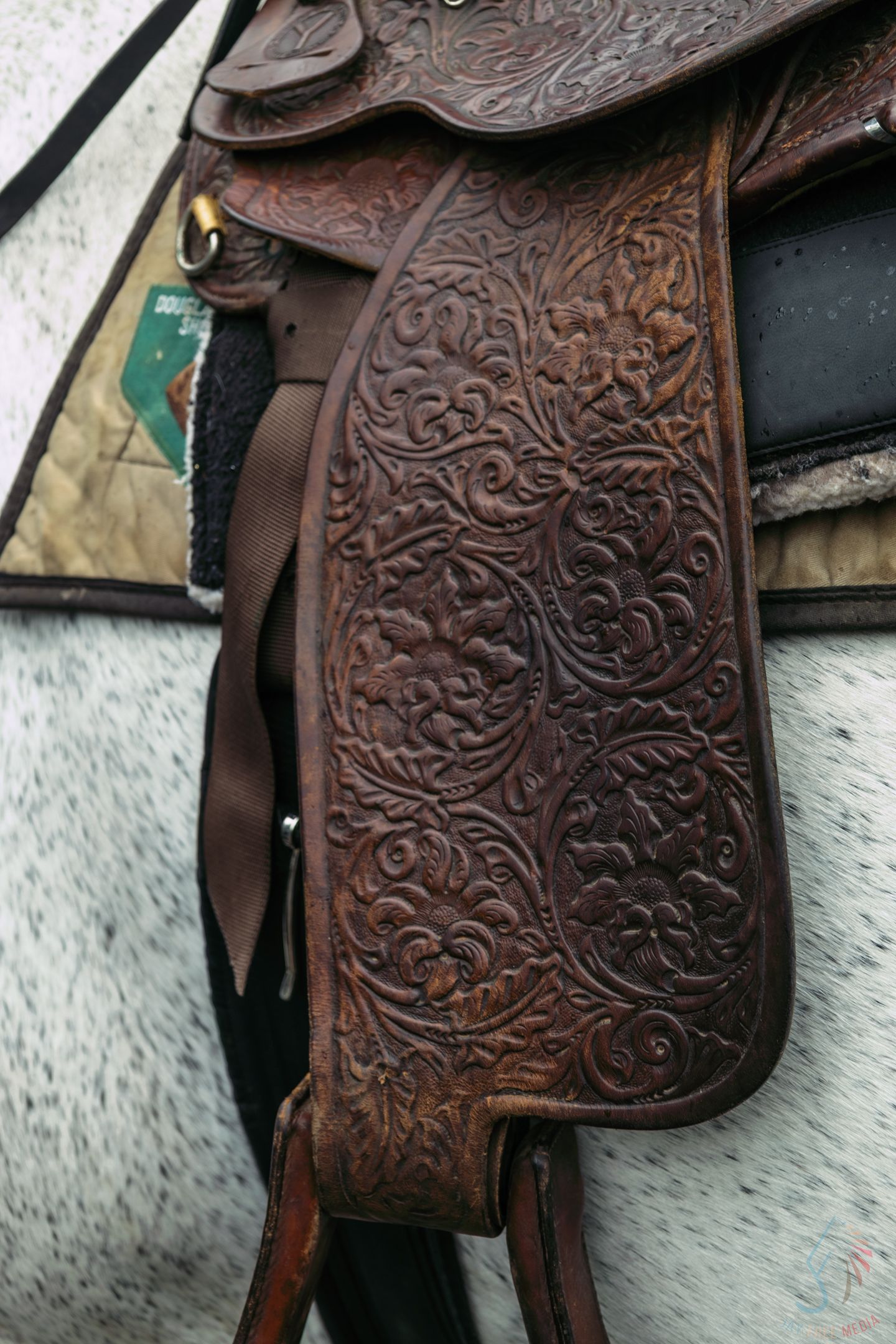 Close-up of ornate floral tooled leather Western saddle on a gray horse.