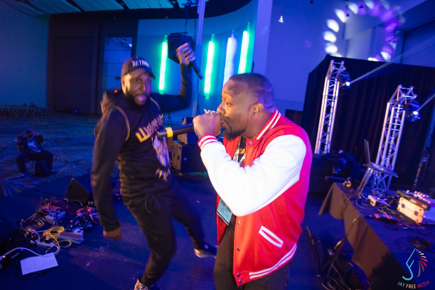 Two performers rap on stage with colorful neon lights and DJ equipment at a live hip-hop concert event.