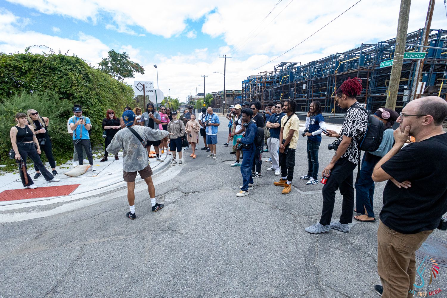Diverse crowd gathered outdoors near colorful stacked crates during a street event on a sunny day.