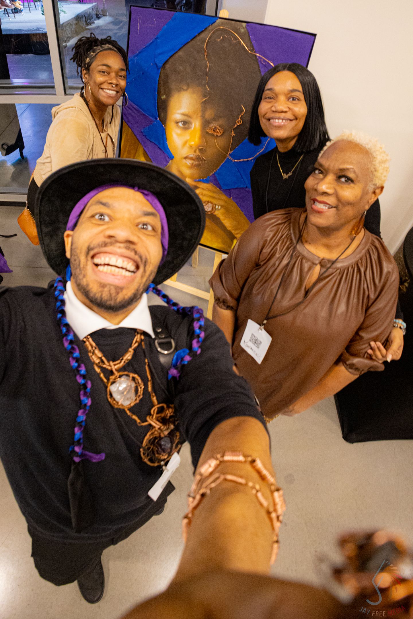 Group takes joyful selfie at art gallery event with colorful portrait paintings displayed in background.