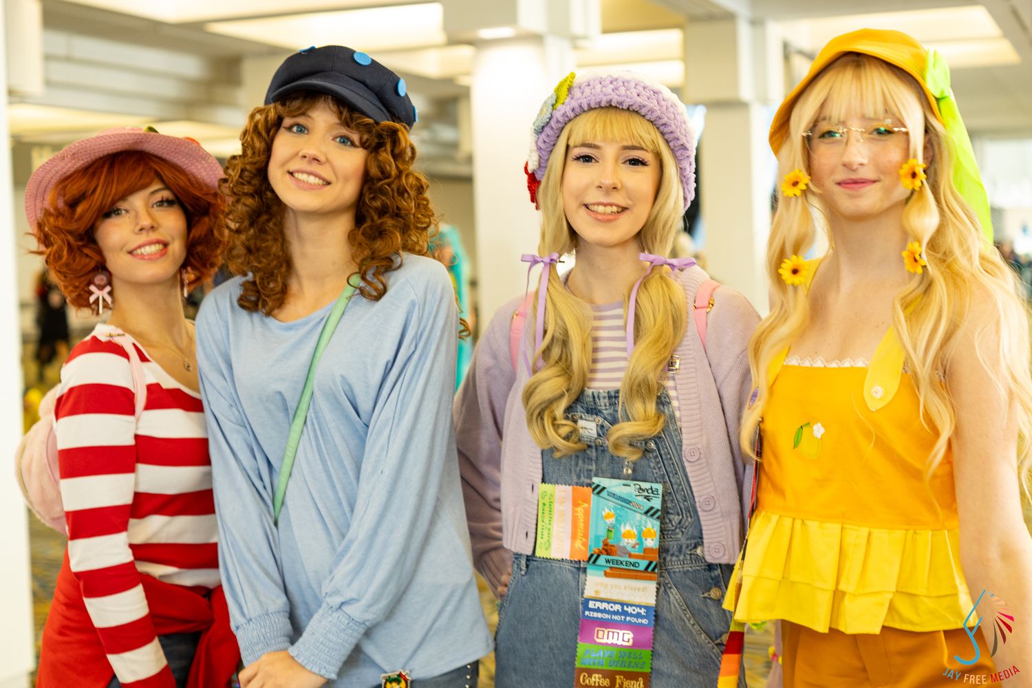 Four women in colorful group cosplay costumes smiling together at a convention.