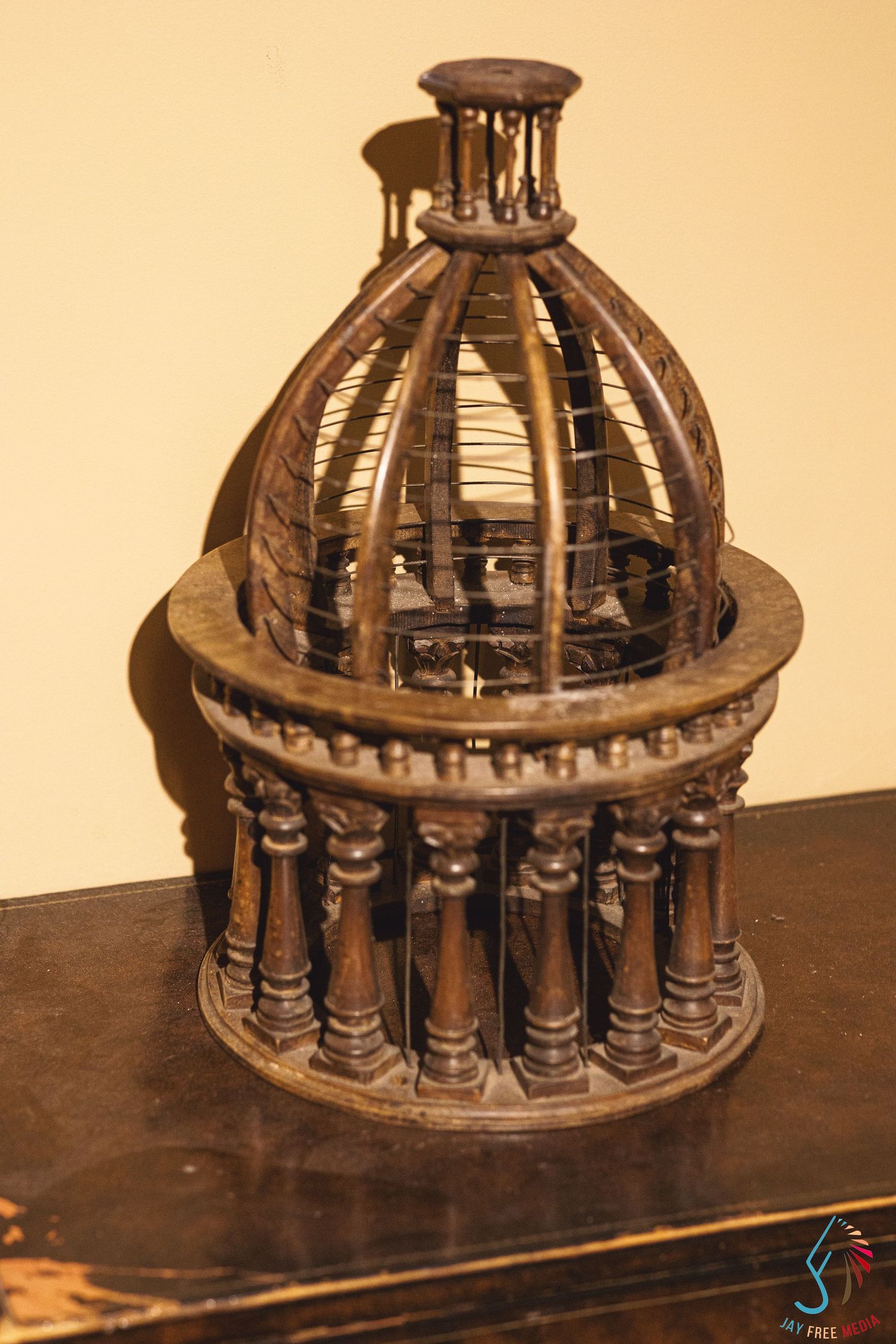 Antique wooden birdcage with dome top and decorative columns displayed on a dark wooden surface.