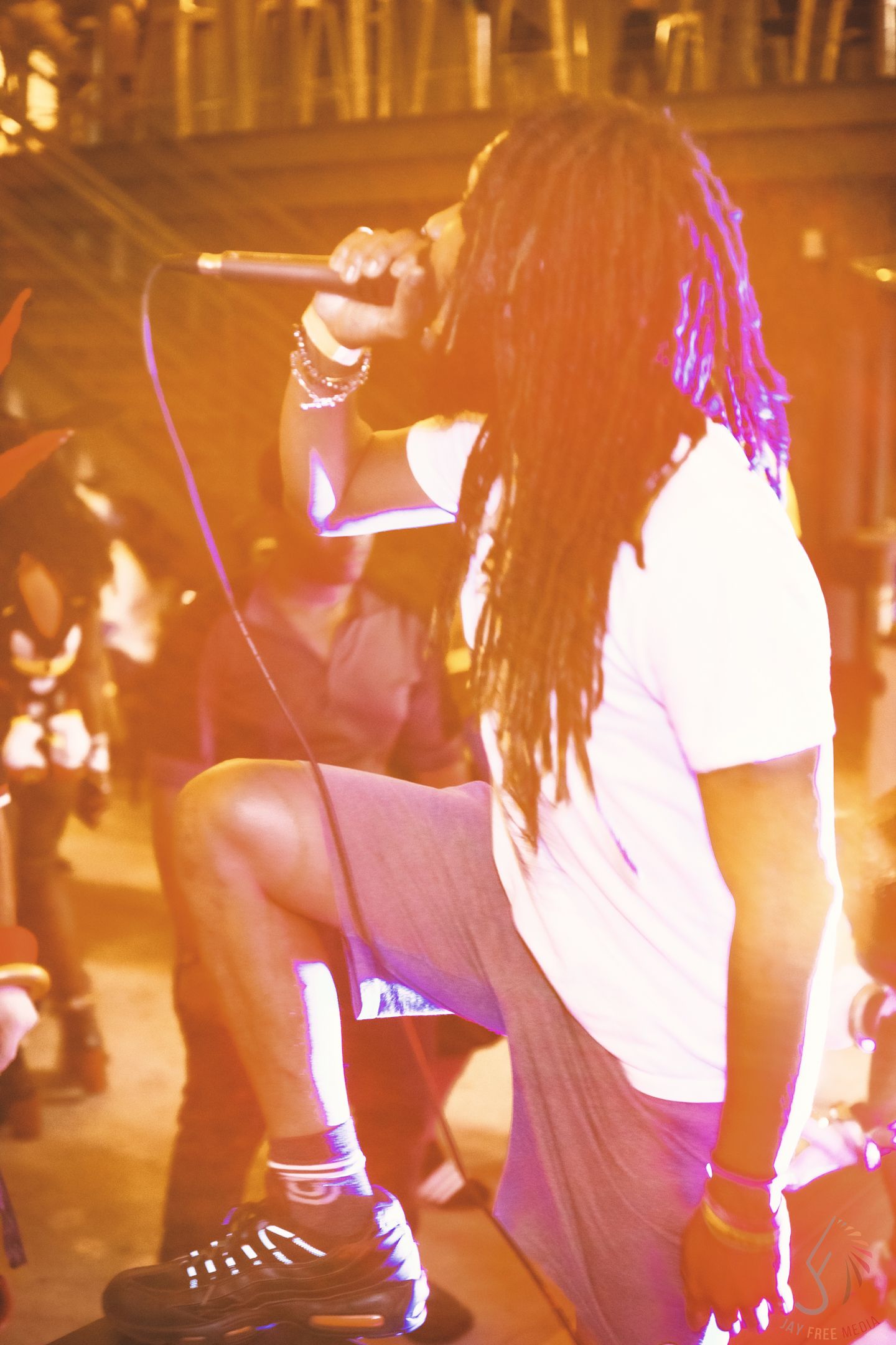 Performer with long dreadlocks singing into a microphone on stage under warm orange lighting.