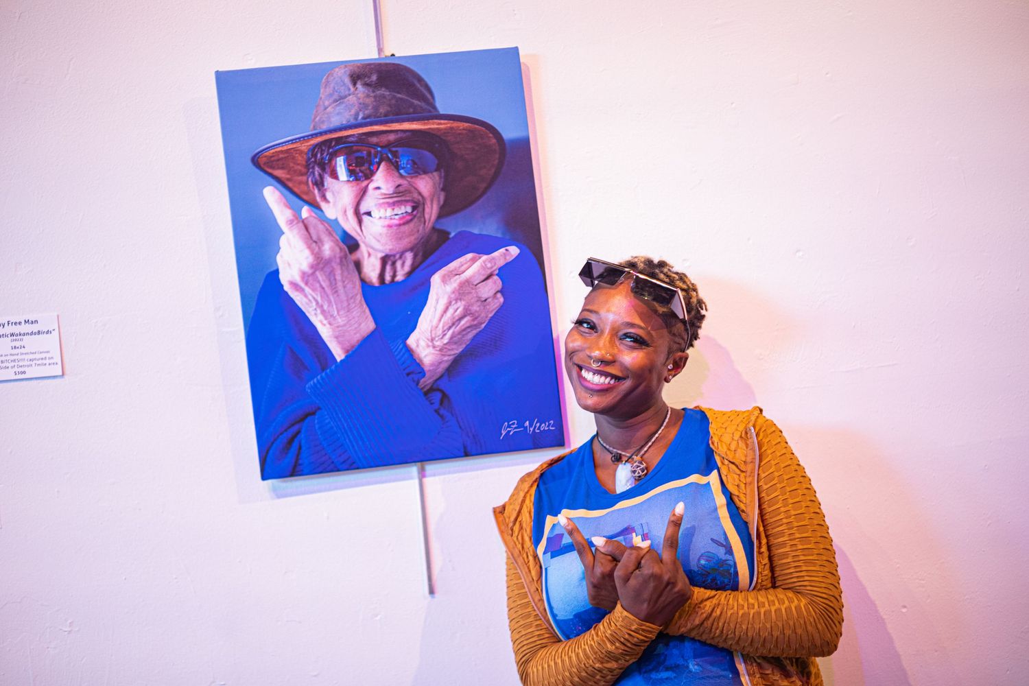 Woman smiling beside a vibrant blue portrait painting at an art gallery exhibition.