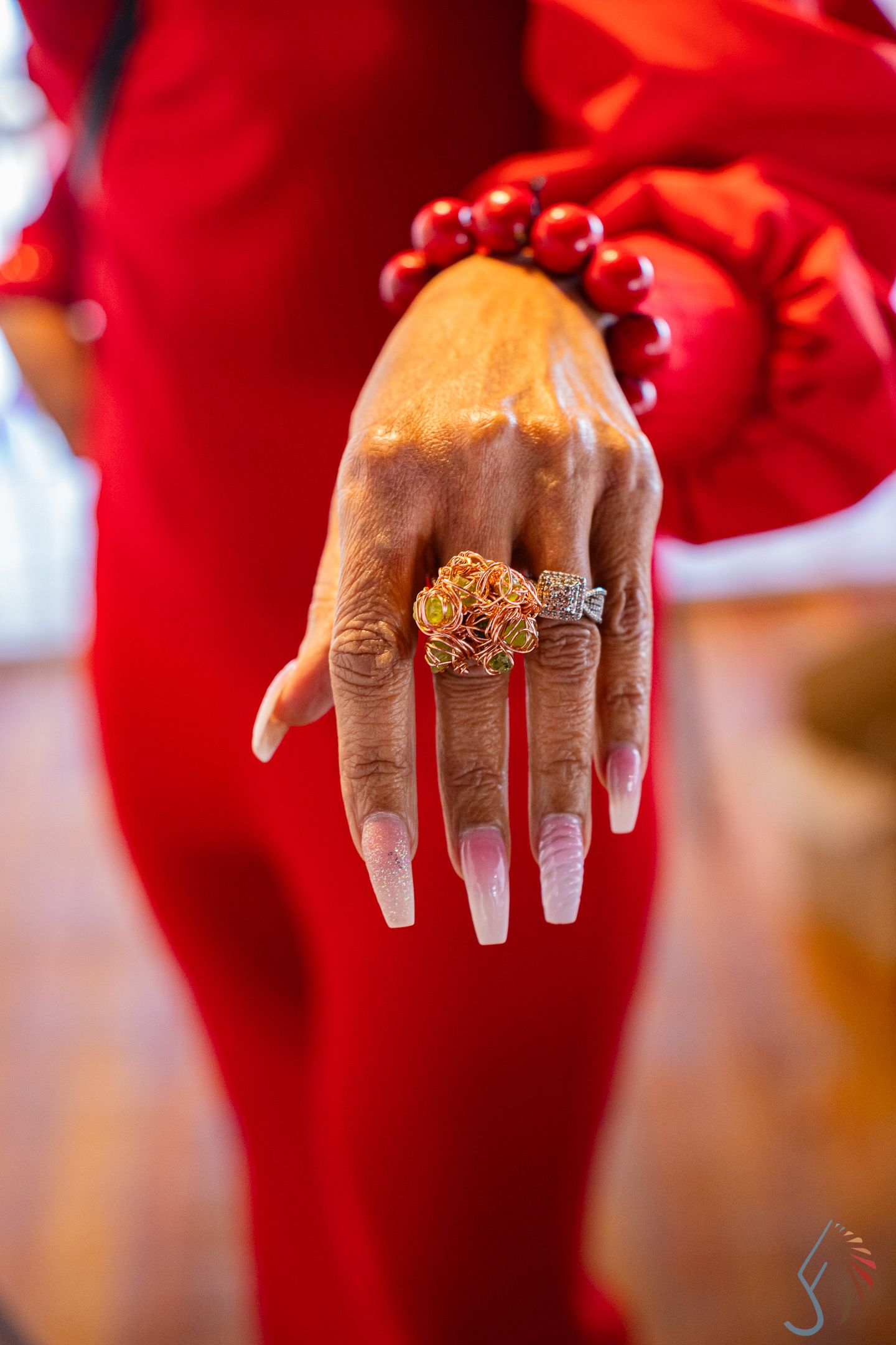 Close-up of a hand with long nails wearing ornate rings and red beaded bracelet.